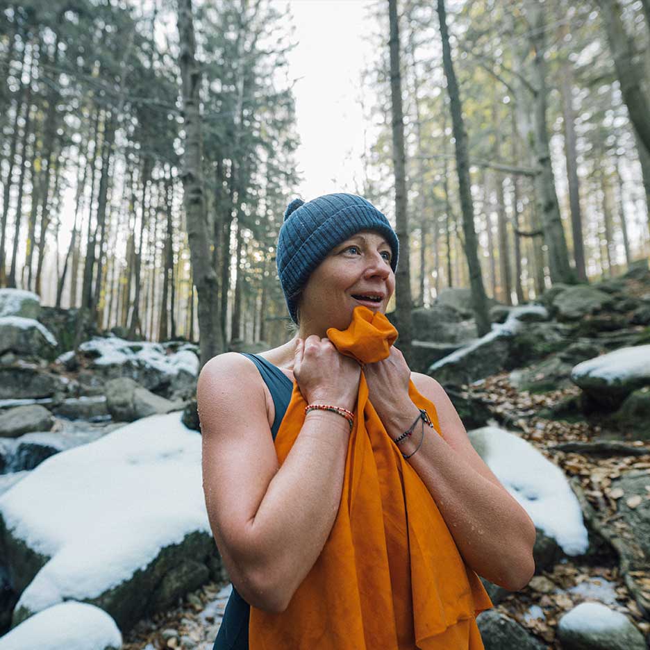 Donna con berretto e costume da bagno che si riscalda con un asciugamano in una foresta innevata.