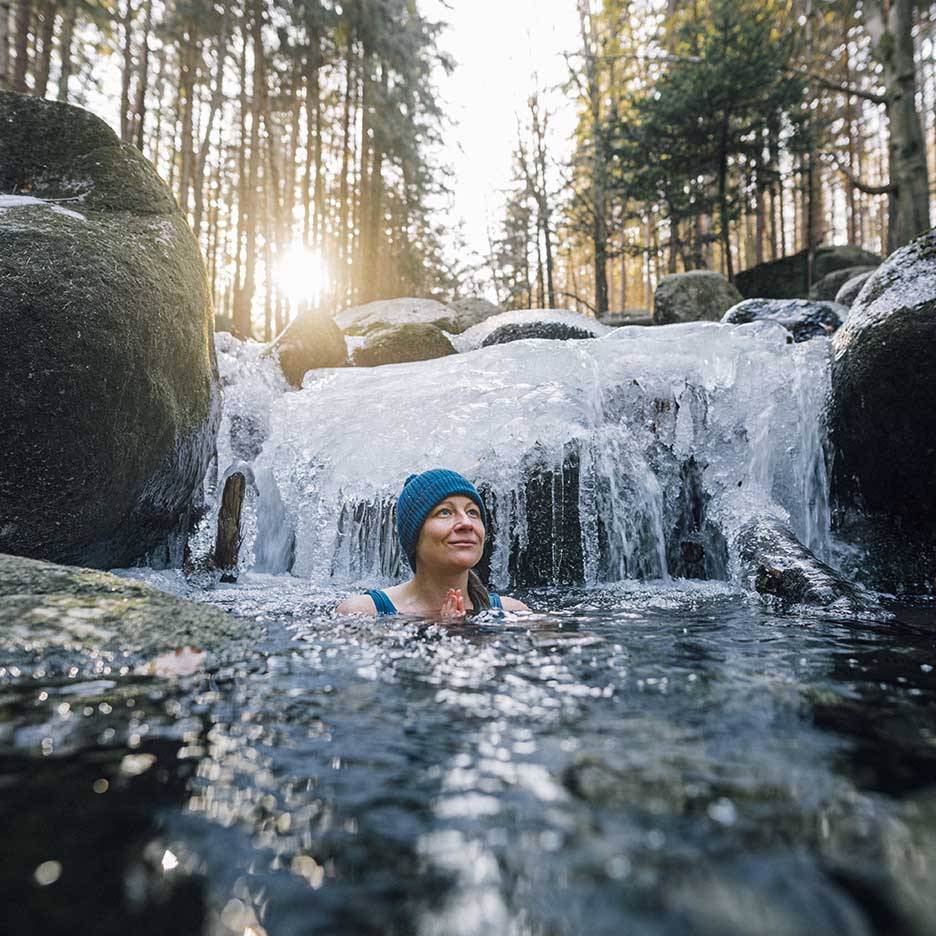 Donna con cappello e costume da bagno blu che si gode un bagno freddo in un fiume ghiacciato.