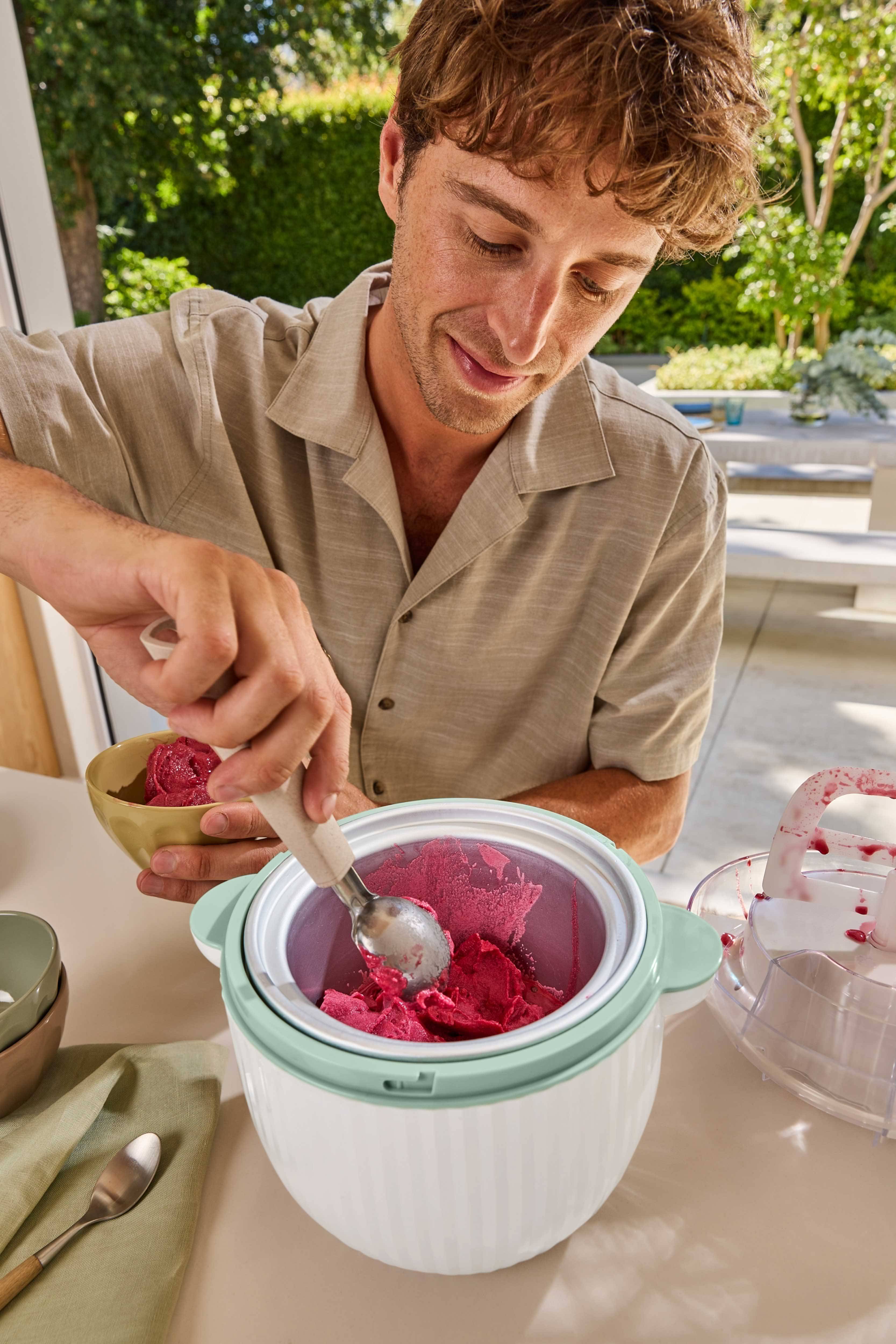 Uomo che serve sorbetto rosso da una gelatiera in una ciotola.