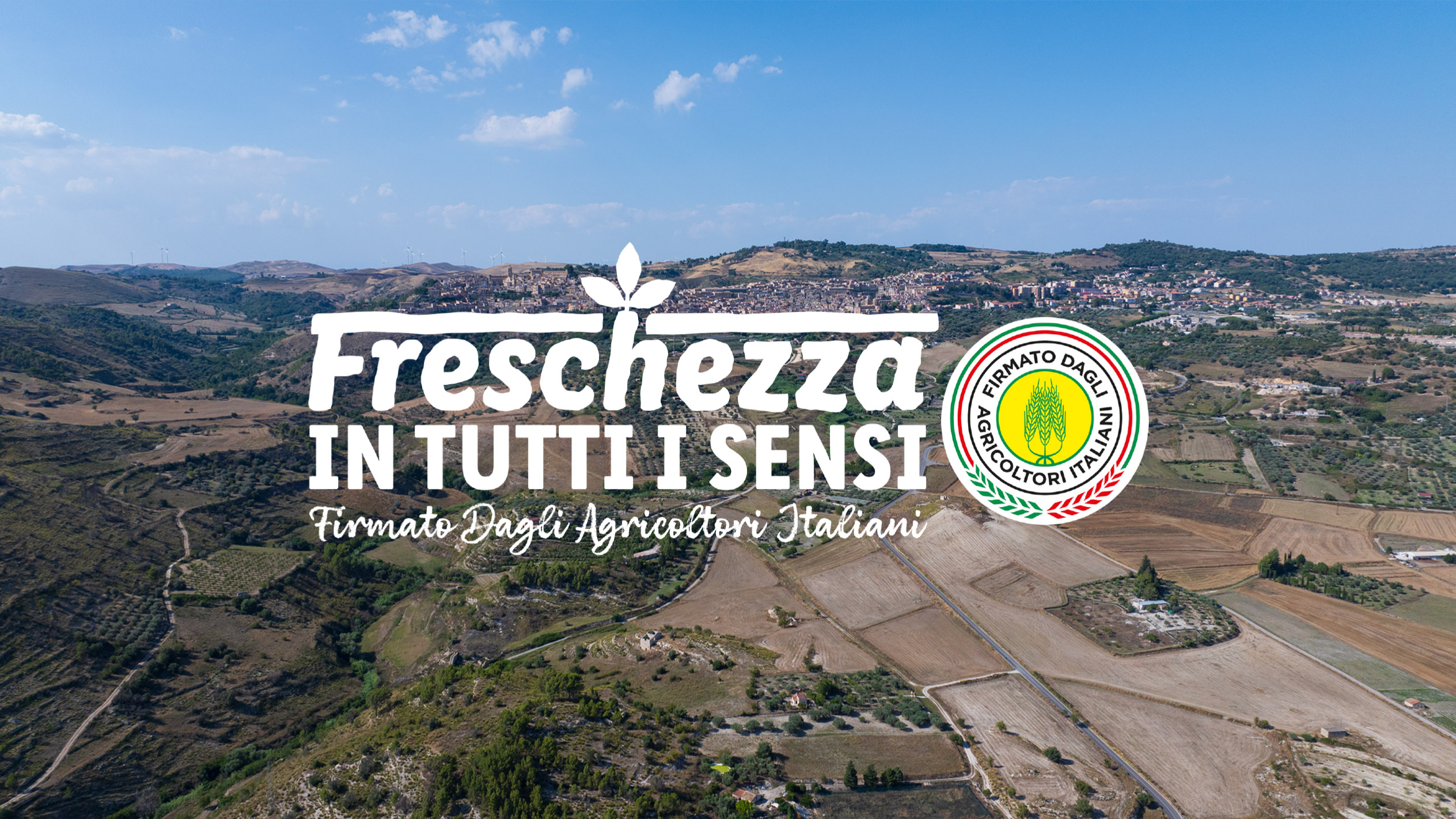 Paesaggio rurale italiano con testo bianco 'Freschezza in tutti i sensi' e logo degli Agricoltori Italiani.