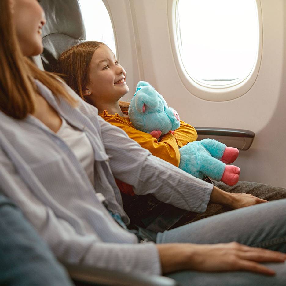 Un bambino con un peluche guarda fuori dal finestrino di un aereo accanto a un adulto.