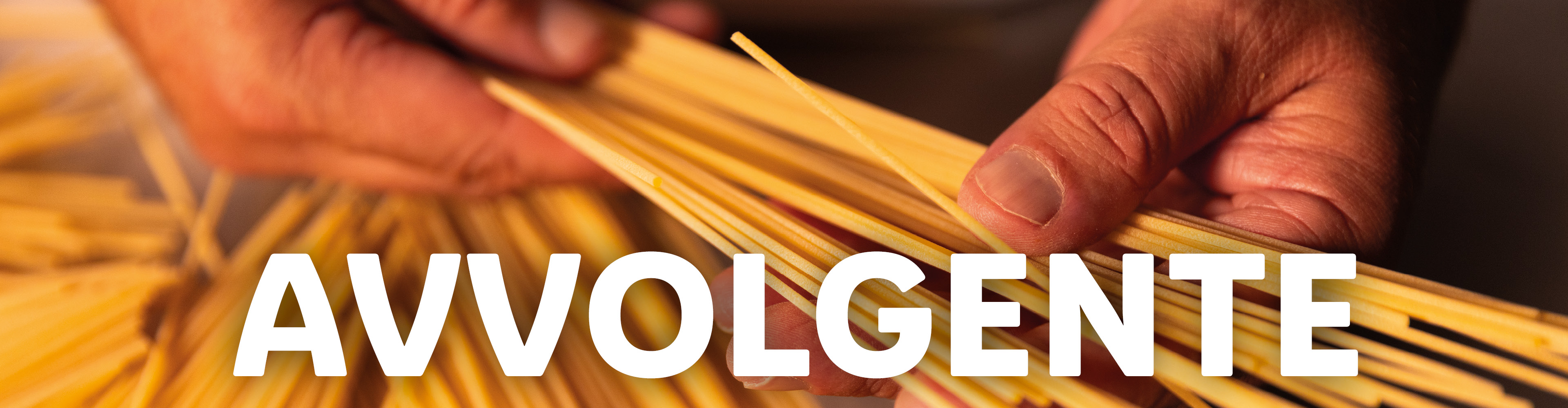 Mani che tengono spaghetti crudi con la scritta 'AVVOLGENTE'.