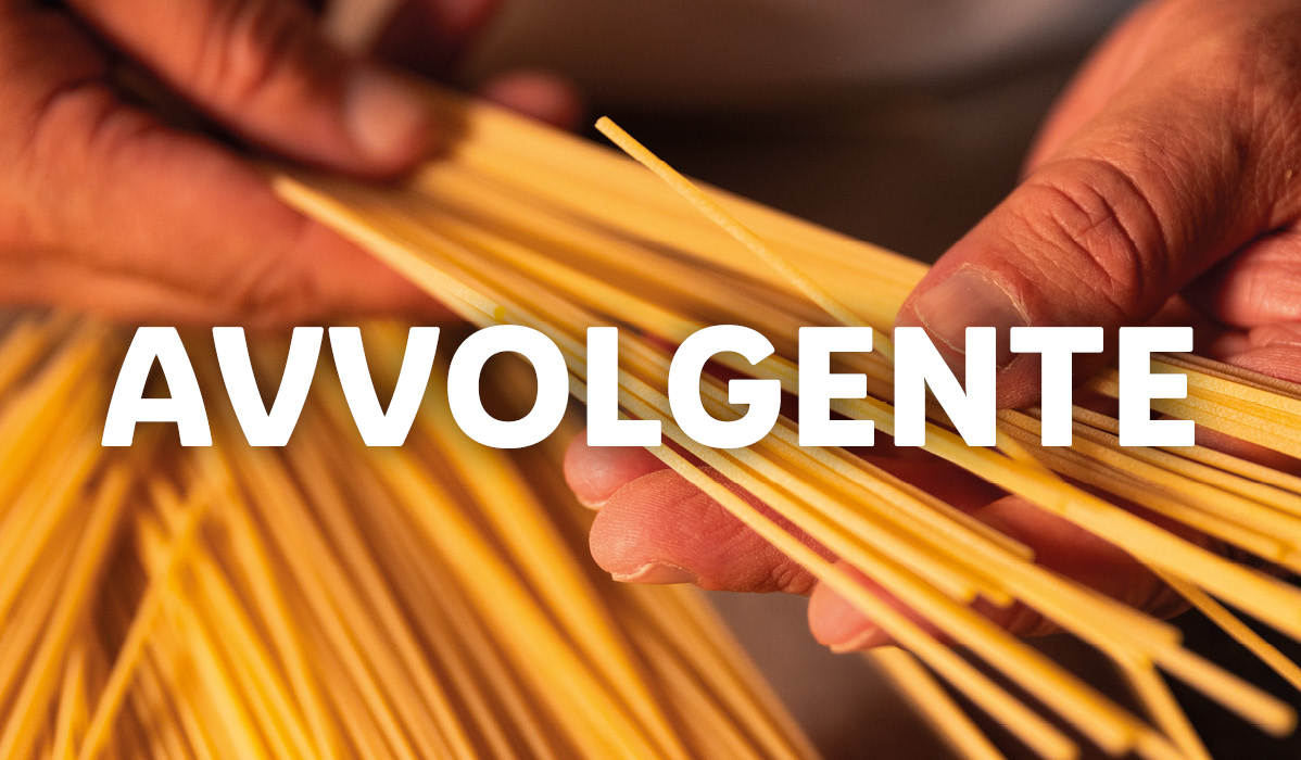 Mani che tengono spaghetti crudi con la scritta 'AVVOLGENTE'.