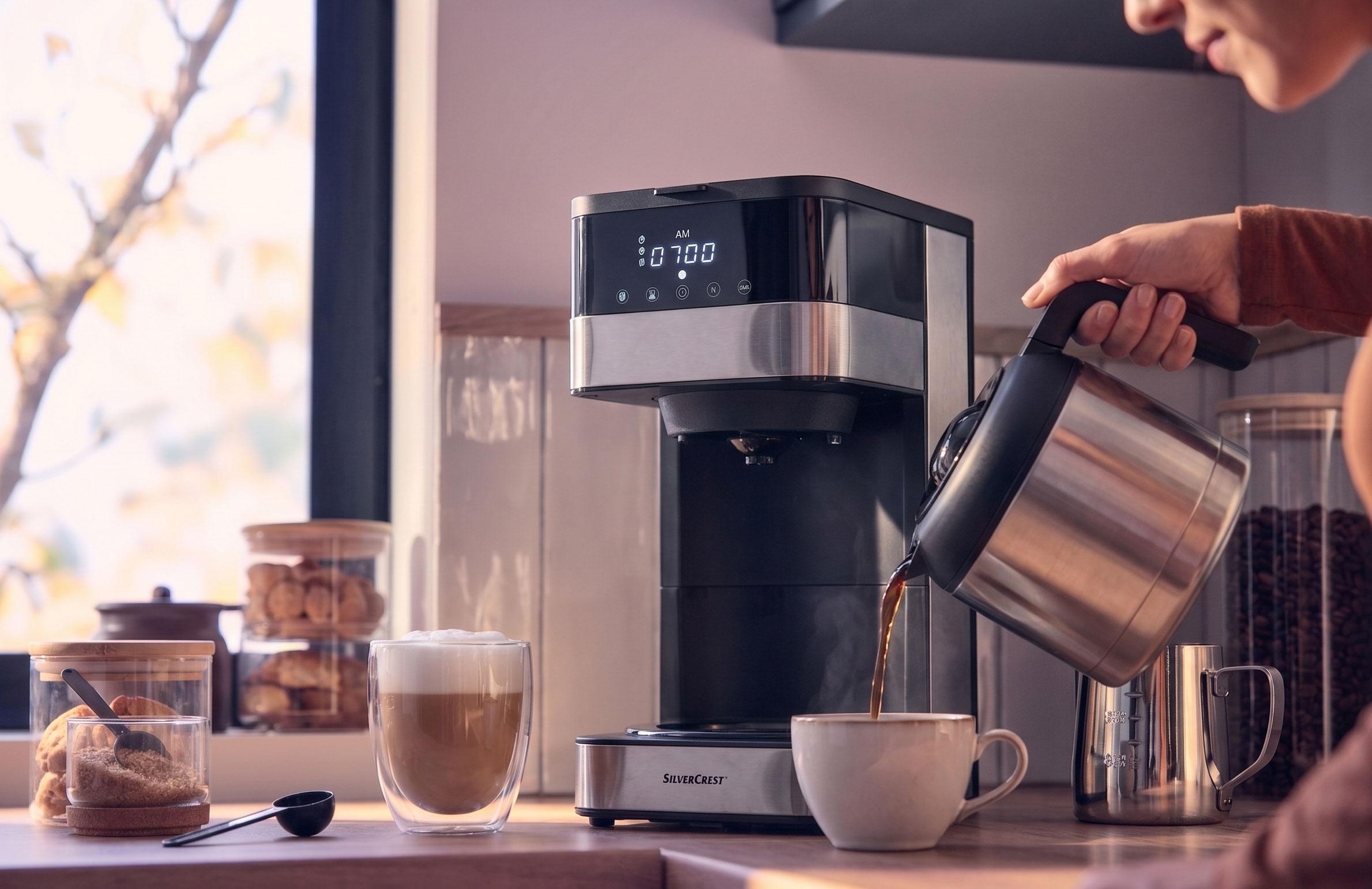 Macchina da caffè che versa caffè in una tazza, con un latte e biscotti sul bancone.