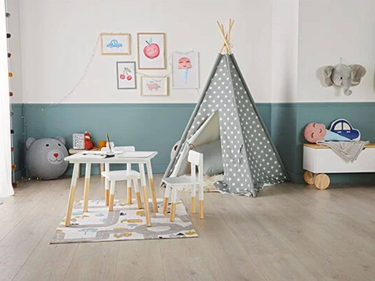 Stanza dei bambini con tenda tipi, tavolo e sedie, baule dei giocattoli e quadri alla parete.