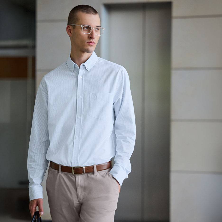 Uomo in camicia a righe azzurra e pantaloni beige con cintura marrone.