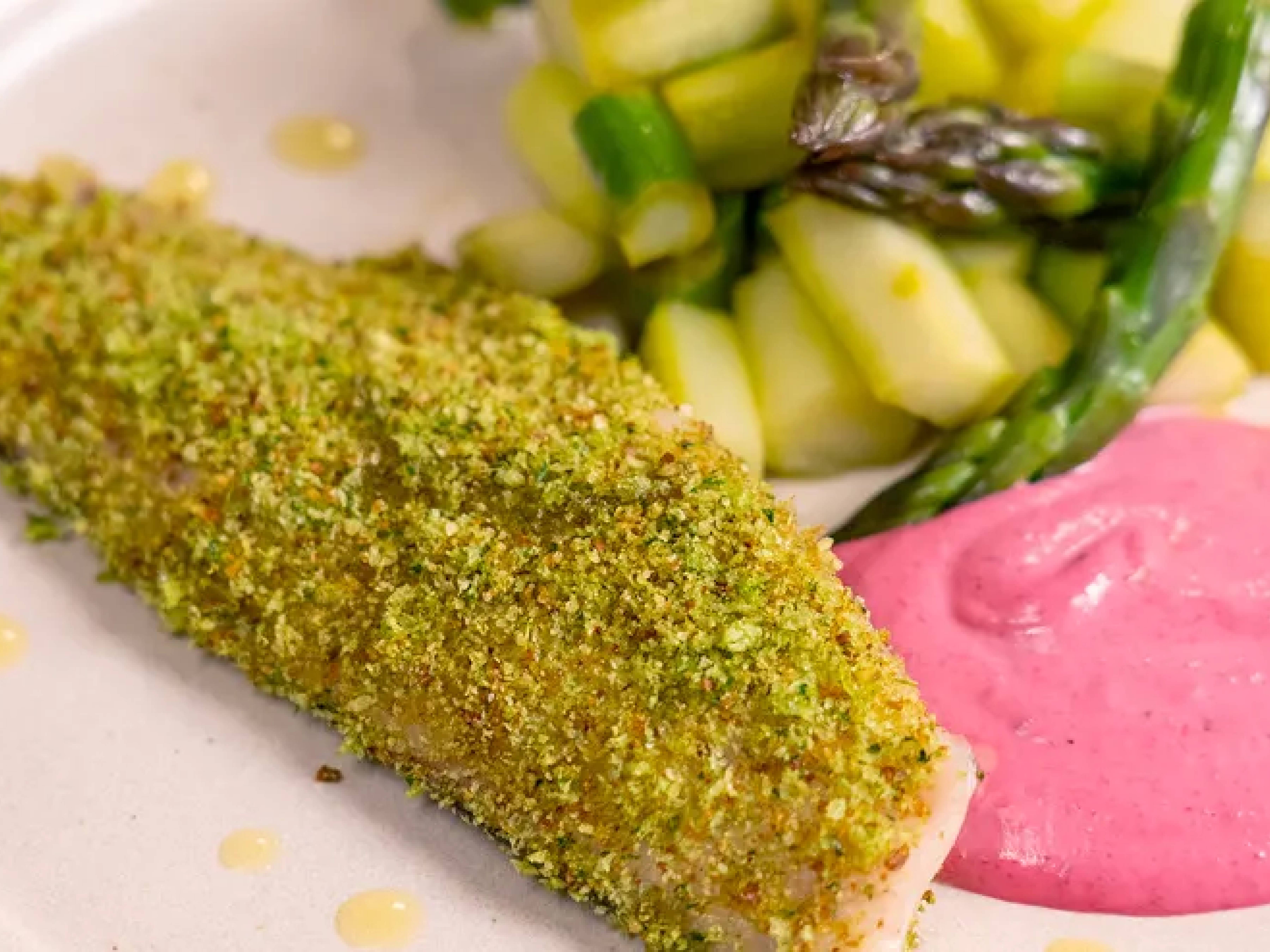 Un filetto di pesce impanato, asparagi e salsa rosa su un piatto bianco.