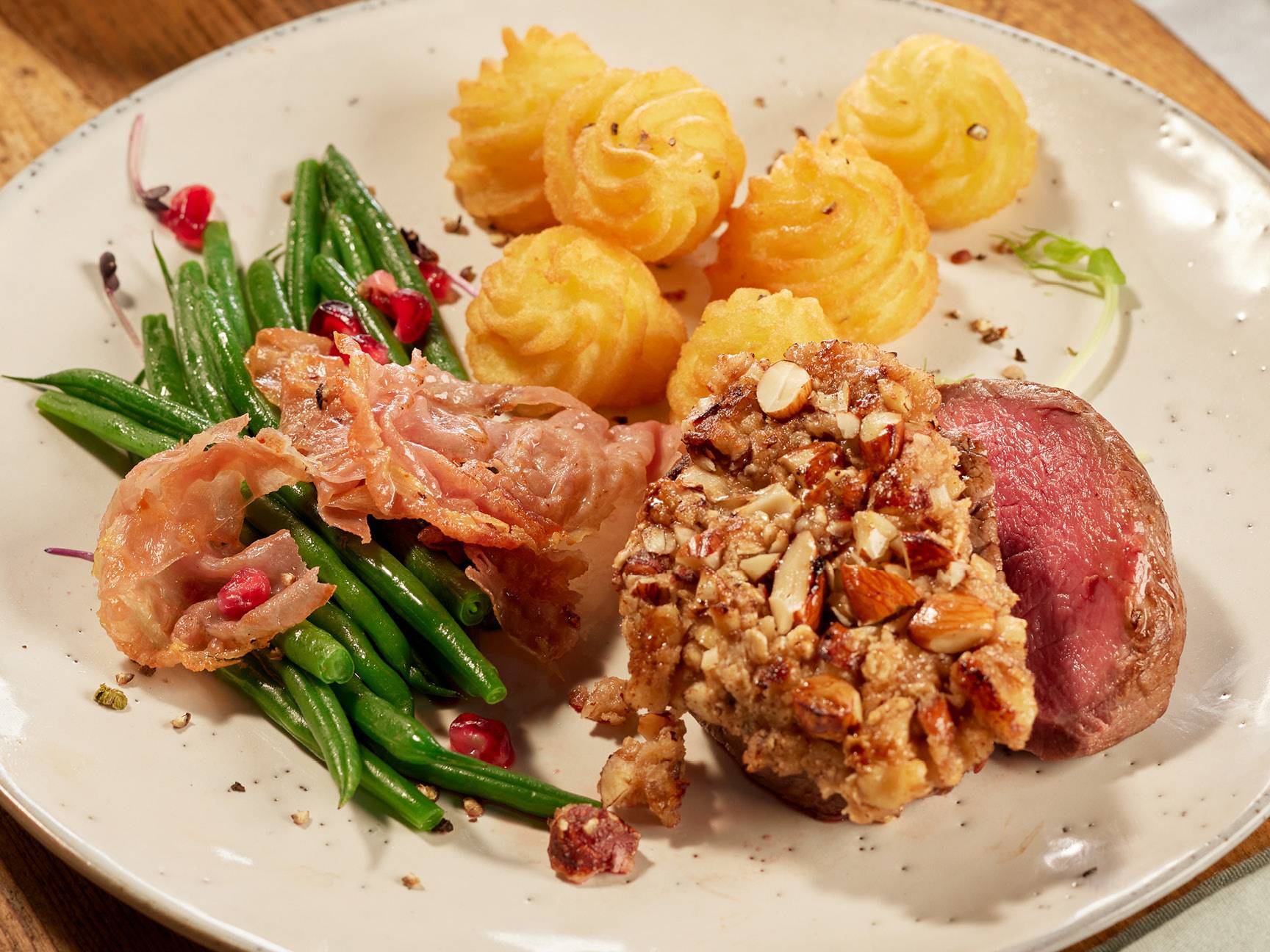 Un piatto di carne con patate duchesse, fagiolini e prosciutto croccante.