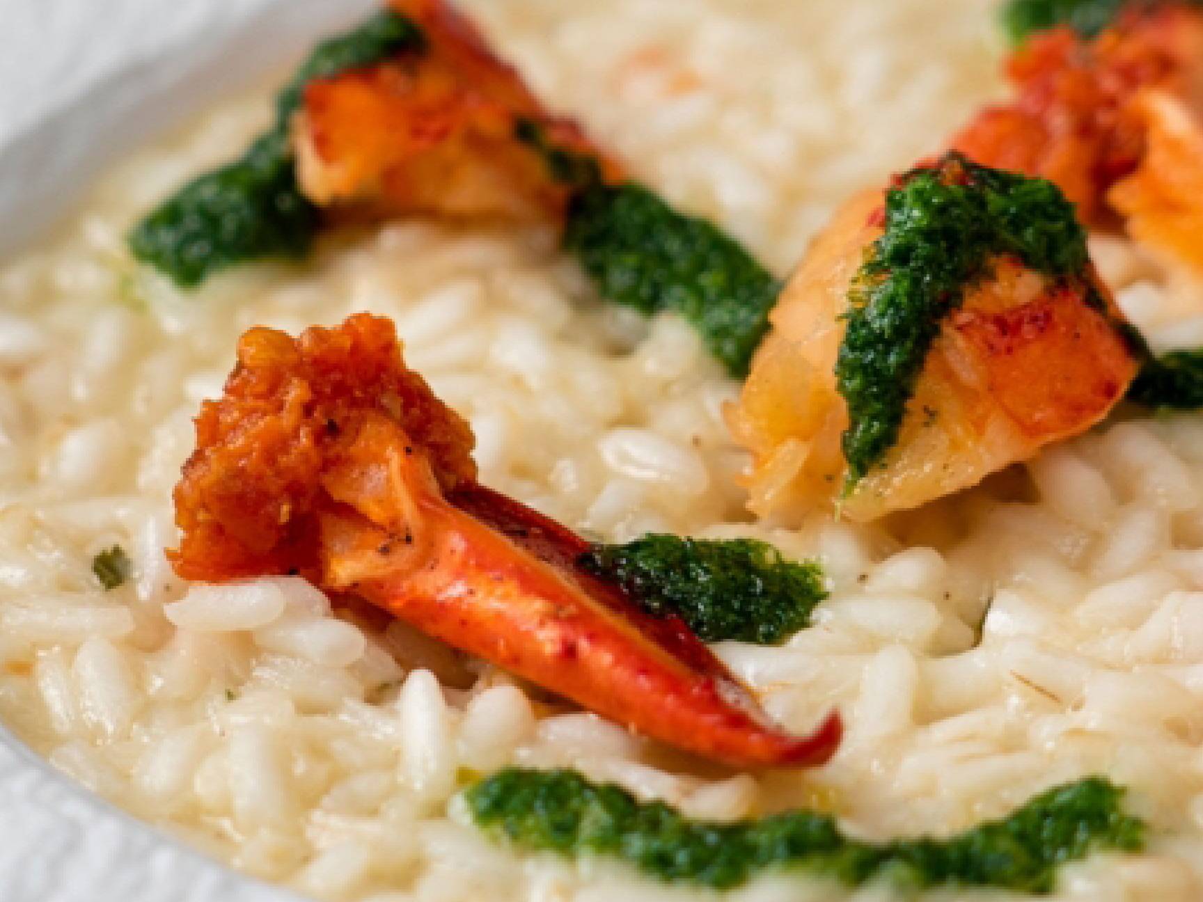 Risotto cremoso con pezzi di aragosta e salsa verde.