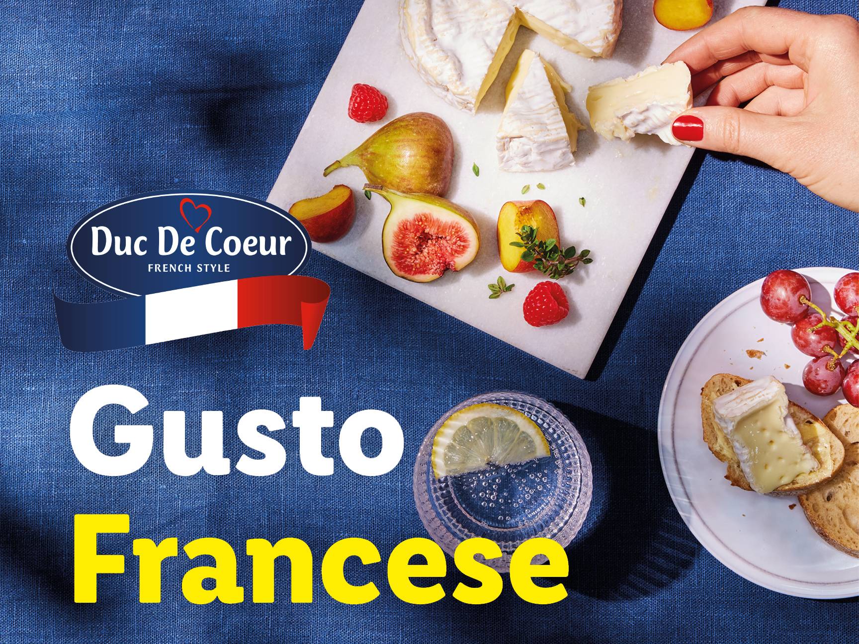 Formaggio Duc De Coeur, frutta e bevande su un tavolo blu.