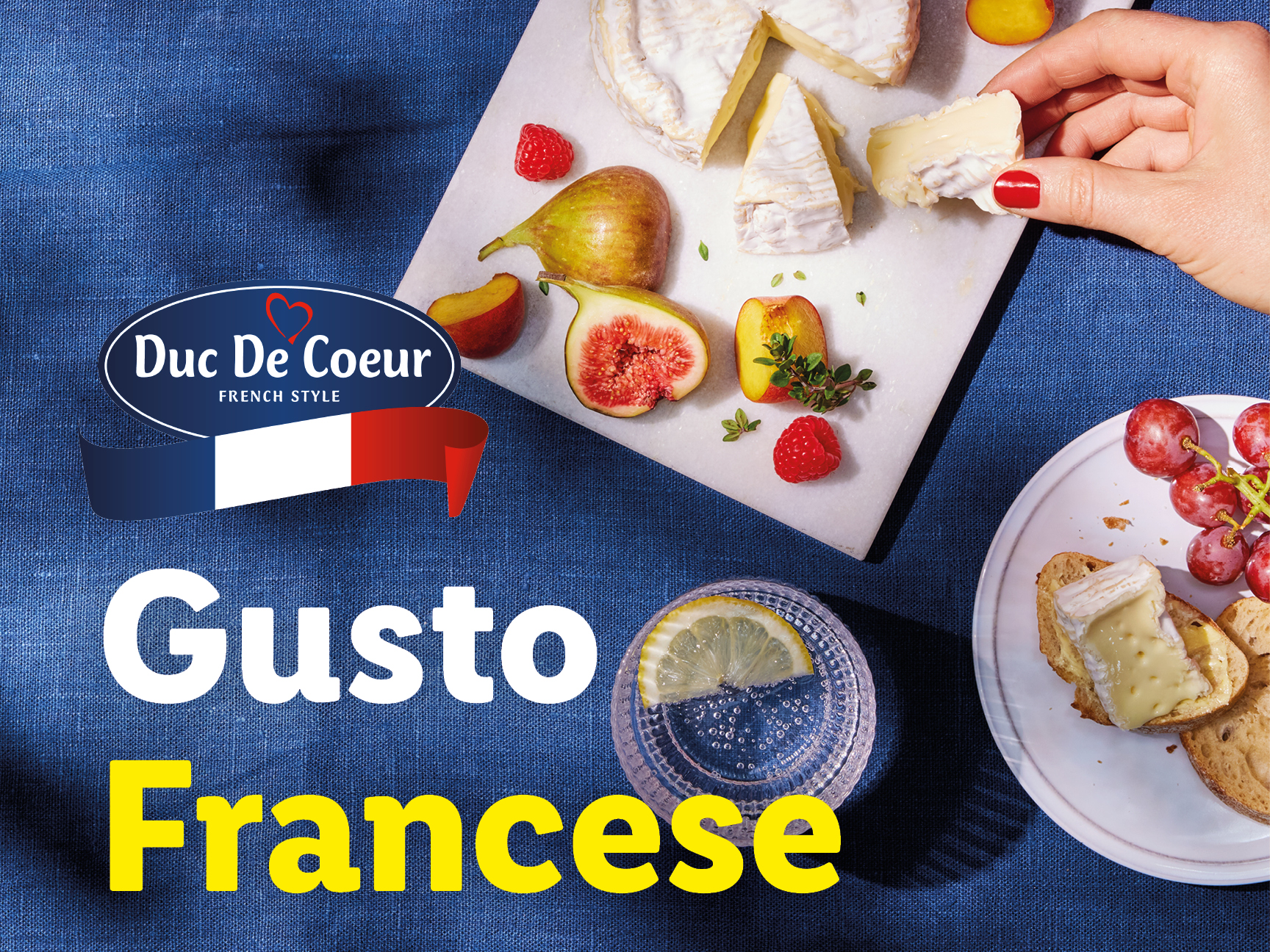 Formaggio Duc De Coeur, frutta e bevande su un tavolo blu.