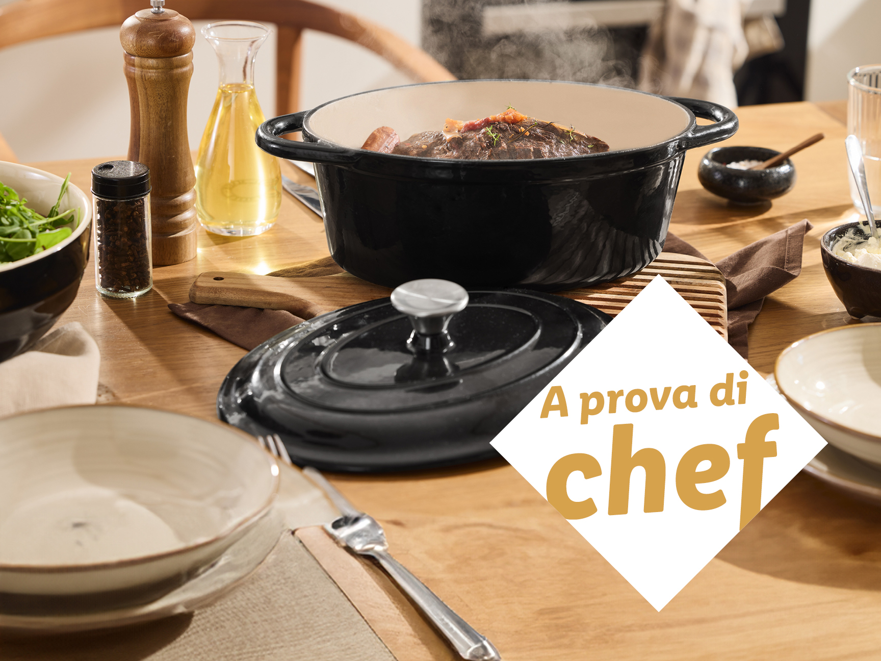 Una pentola in ghisa nera con coperchio, spezie e olio su un tavolo di legno.