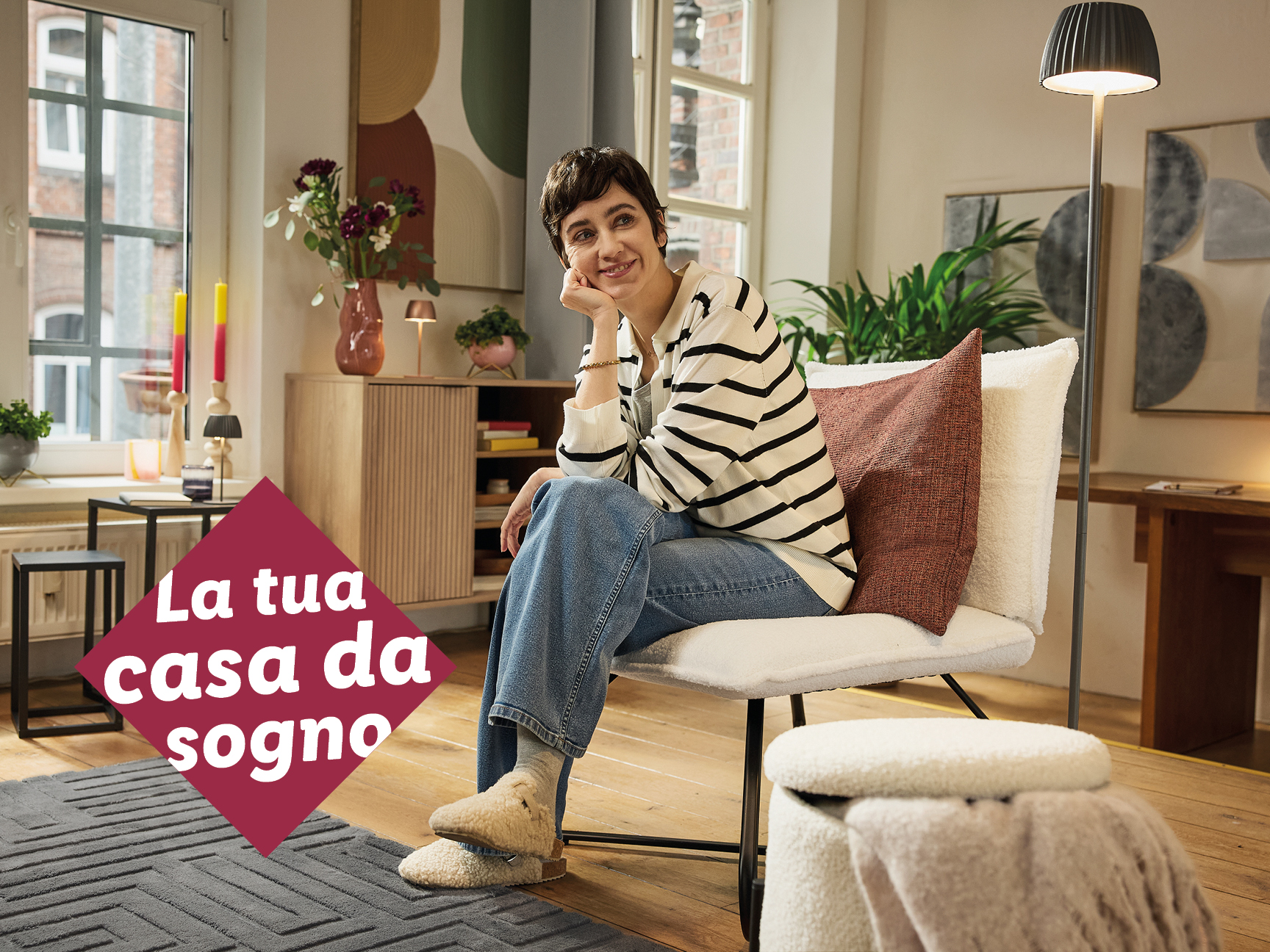 Una donna sorridente seduta su una sedia in un soggiorno accogliente, con un tappeto grigio e mobili in legno.