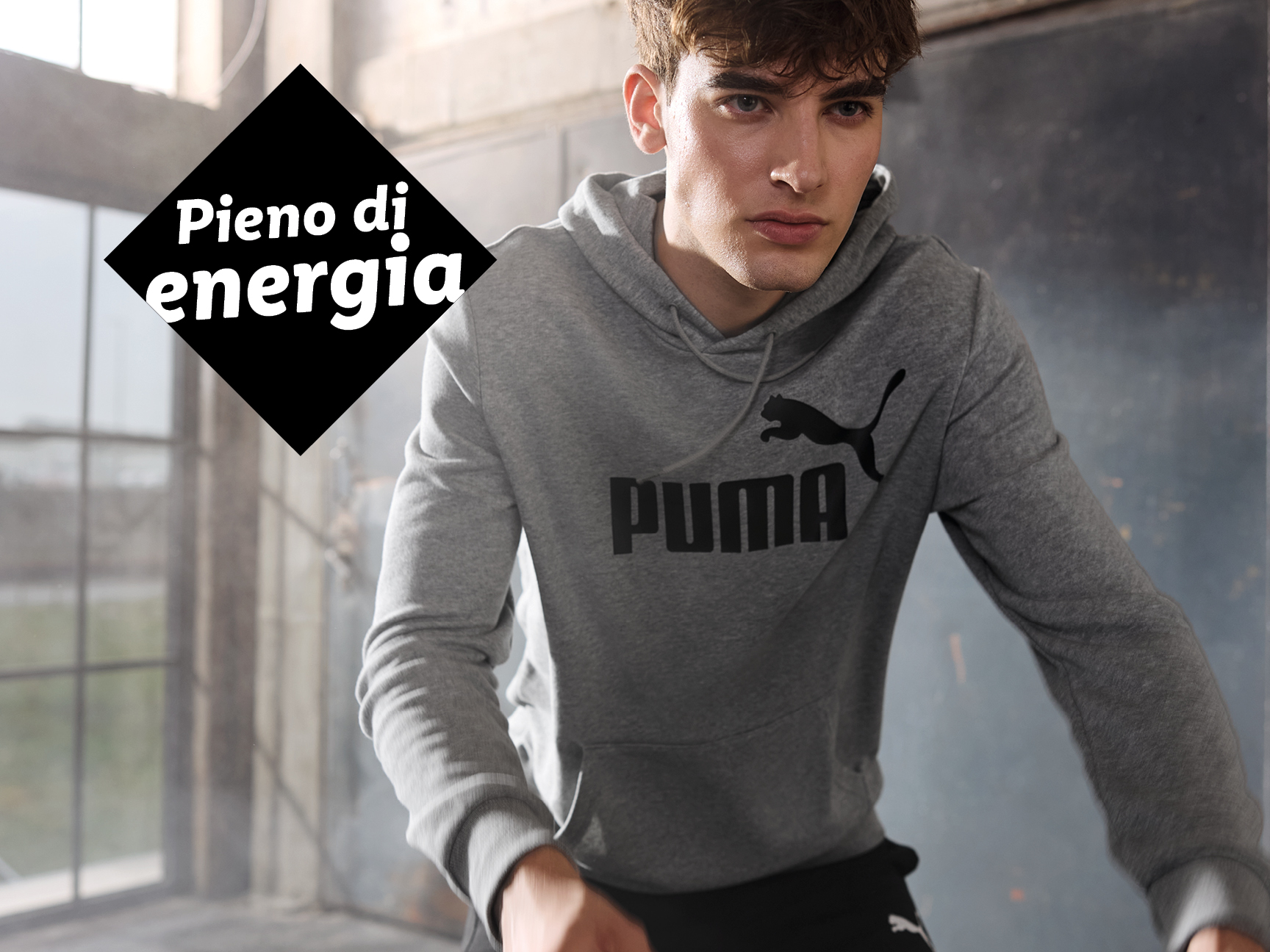 Un uomo indossa una felpa grigia con cappuccio e il logo Puma nero.