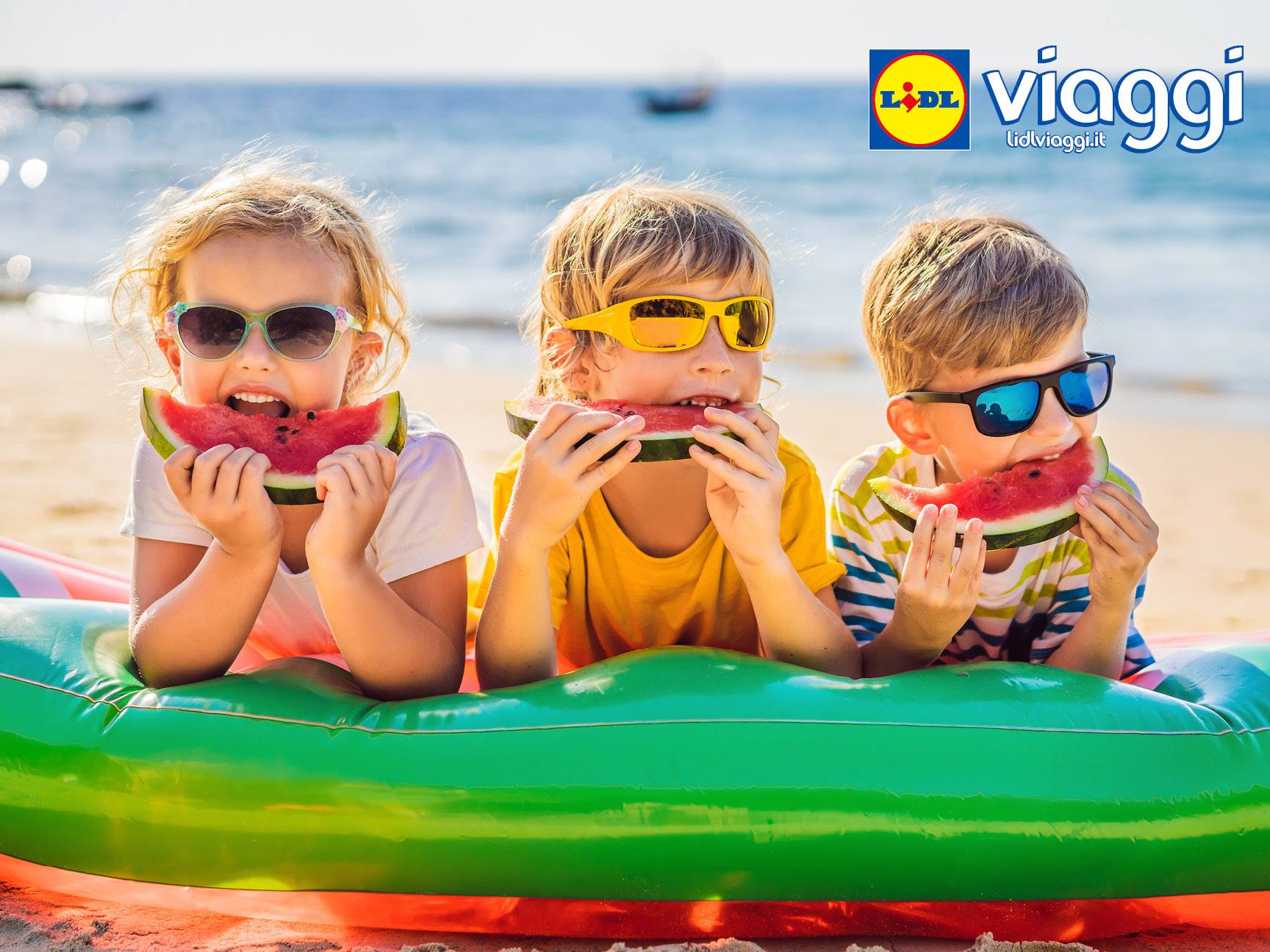 Tre bambini con occhiali da sole mangiano anguria su un gonfiabile in spiaggia, con il logo Lidl Viaggi.