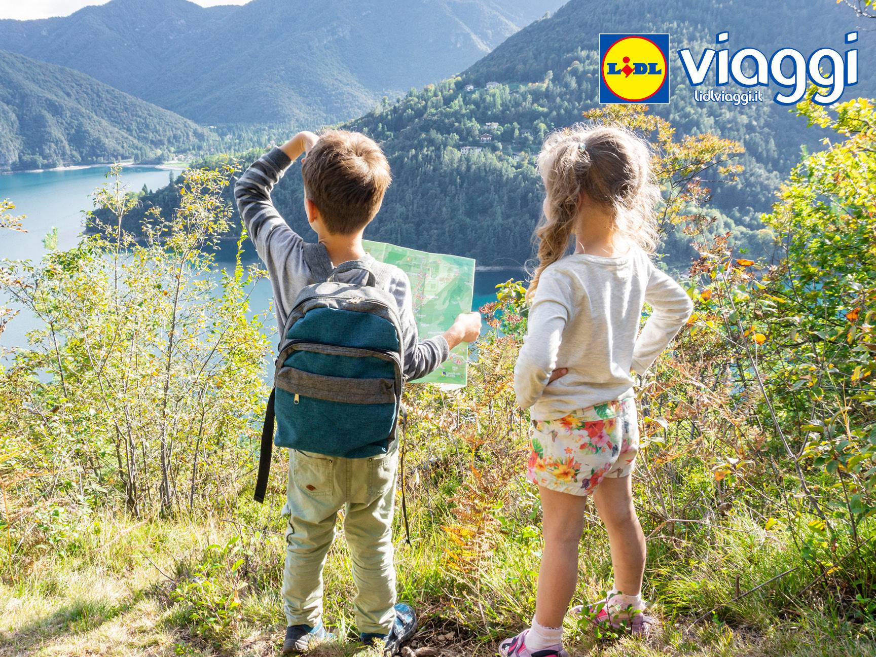 Bambini con zaino e mappa che guardano un lago e montagne, con logo Lidl Viaggi.