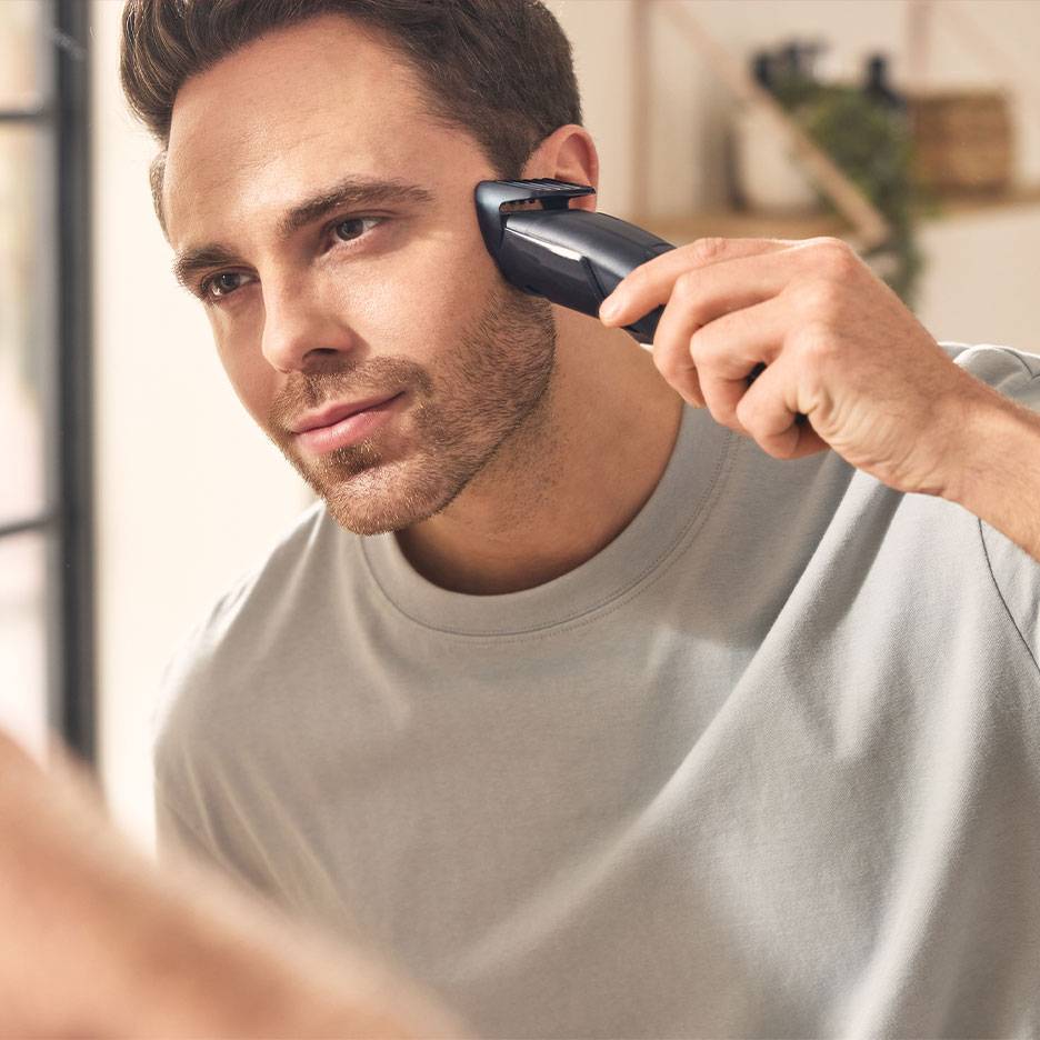 Uomo che si taglia la barba con un rifinitore davanti allo specchio.