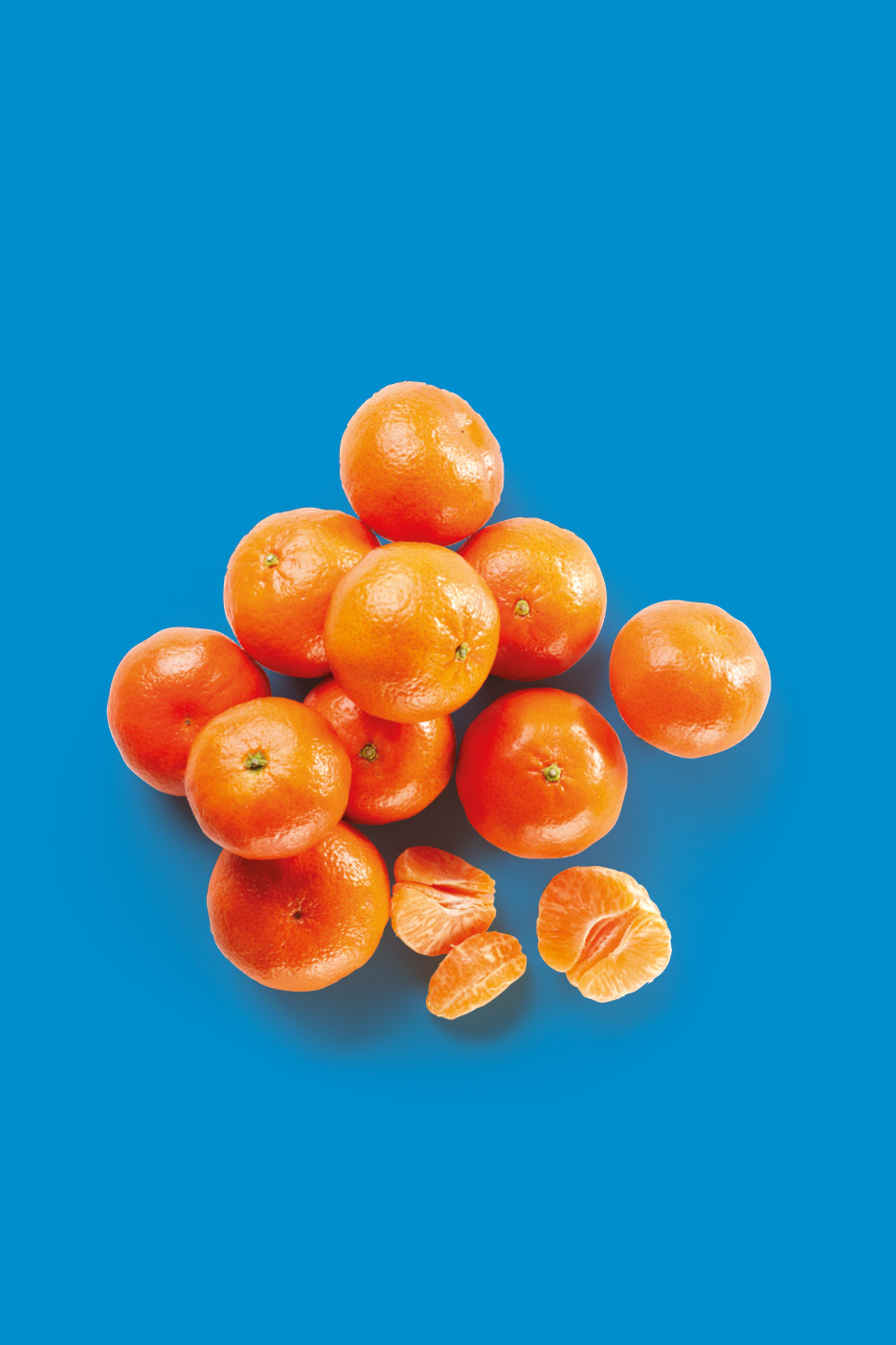 Un mucchio di mandarini interi e alcuni spicchi sbucciati su sfondo blu.