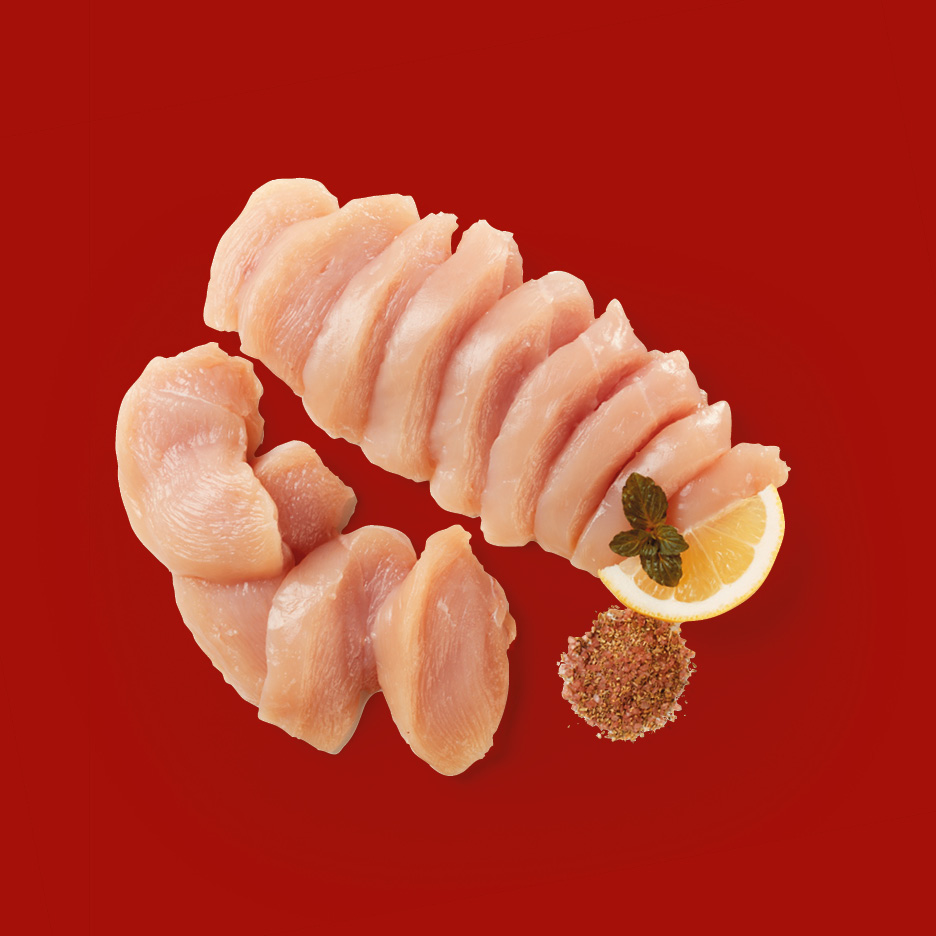 Fette di petto di pollo crudo con limone e spezie su sfondo rosso.