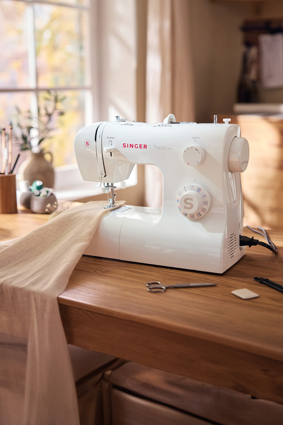 Macchina da cucire Singer Tradition su un tavolo di legno con tessuto e accessori da cucito.