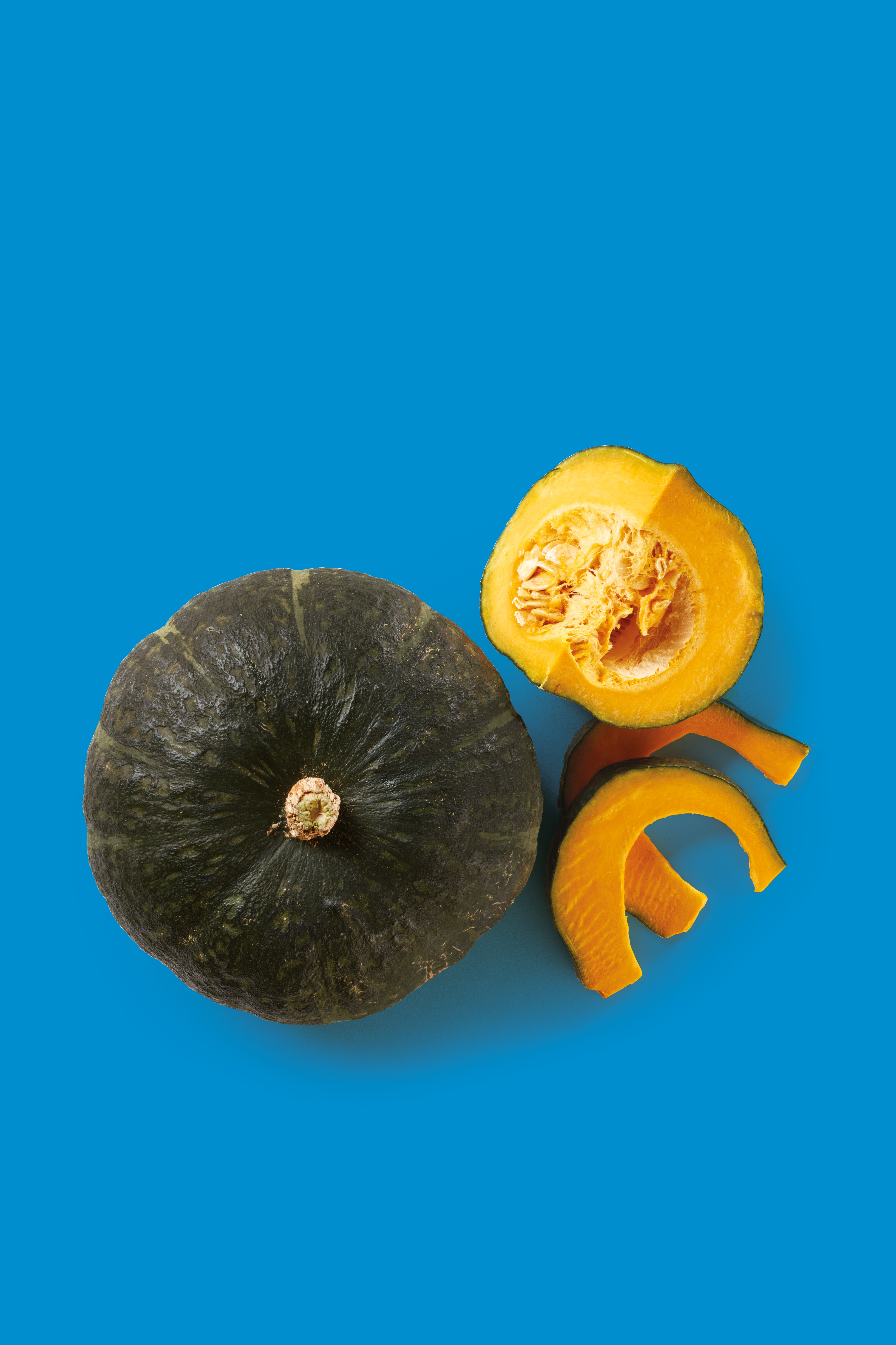 Zucca intera verde scuro e fette di zucca arancioni su sfondo blu.