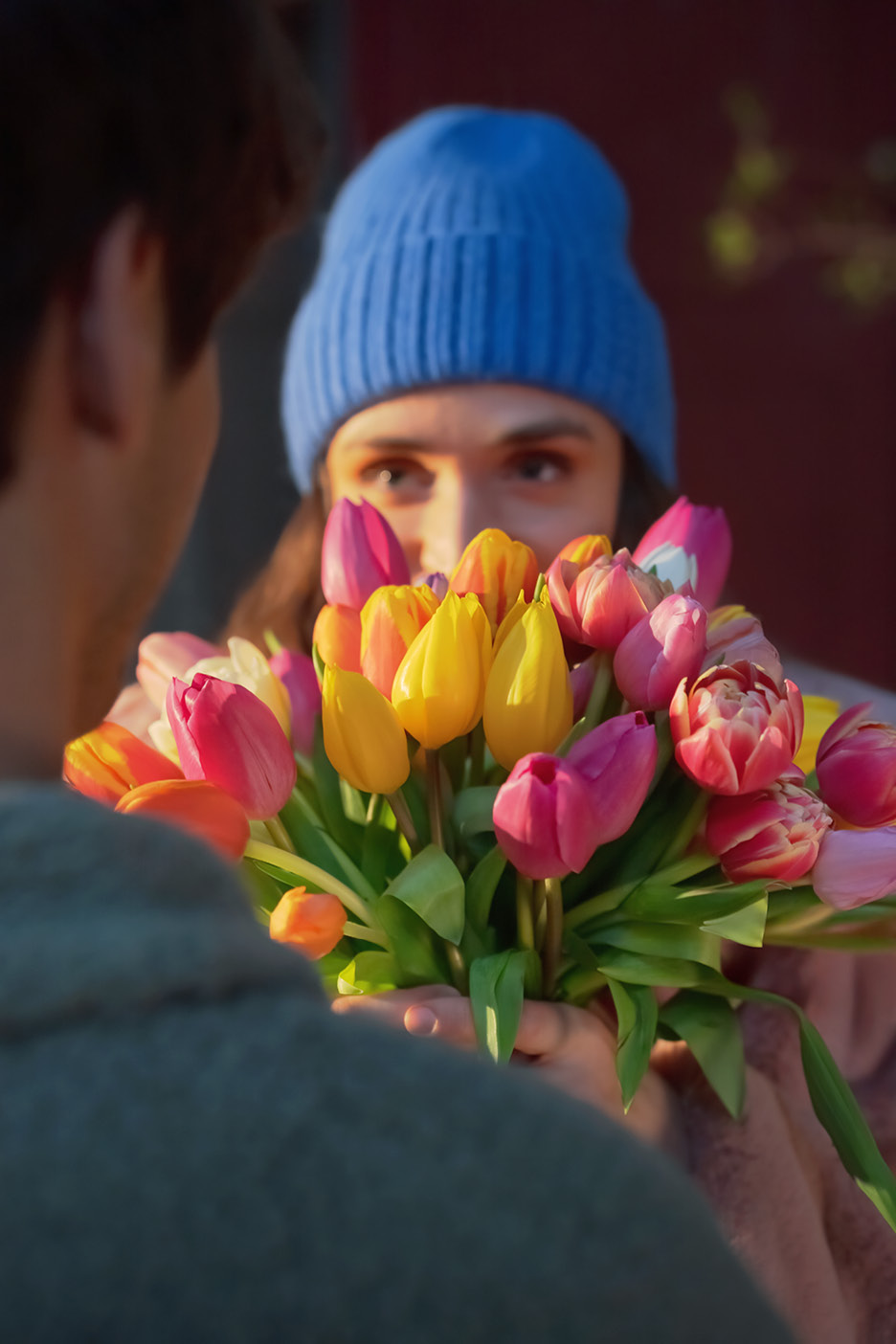 Una persona con un berretto blu offre un bouquet di tulipani colorati a un'altra persona.