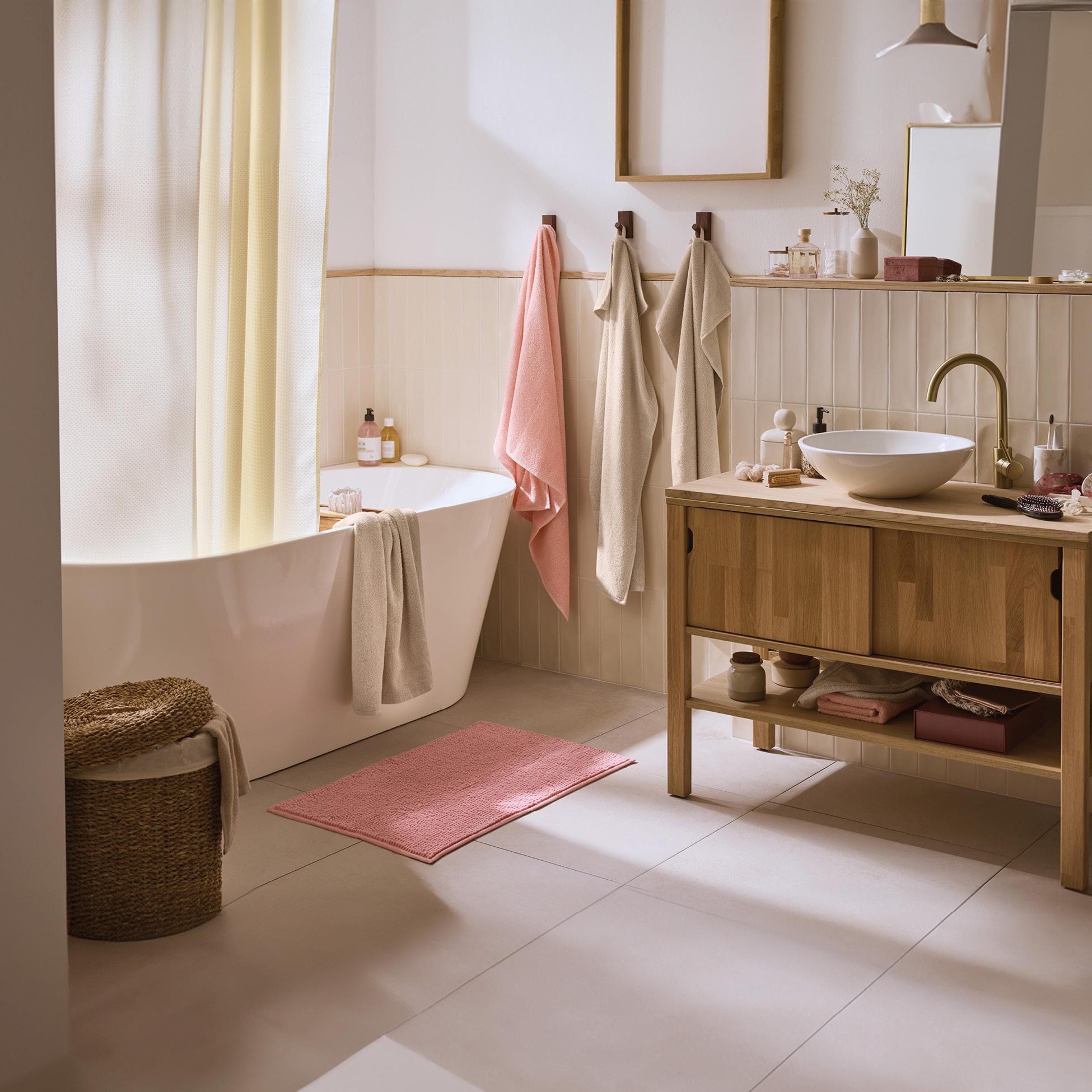 Bagno moderno con vasca bianca, mobile lavabo in legno, asciugamani rosa e beige, e tappeto rosa.