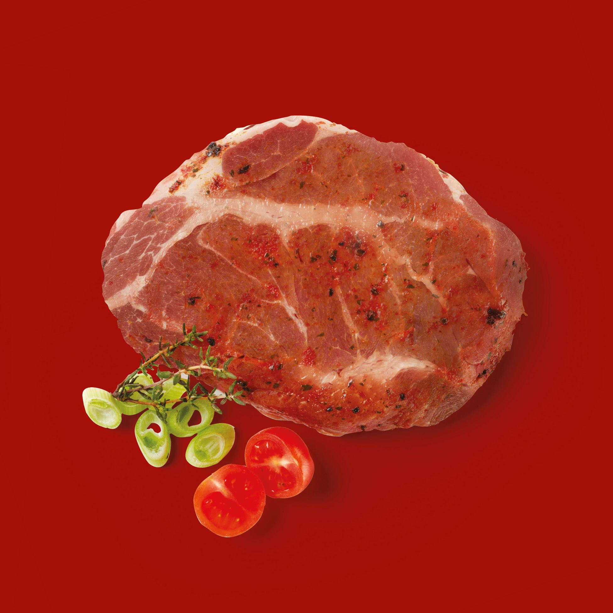 Bistecca di maiale marinata con erbe aromatiche, pomodorini e cipollina su sfondo rosso.