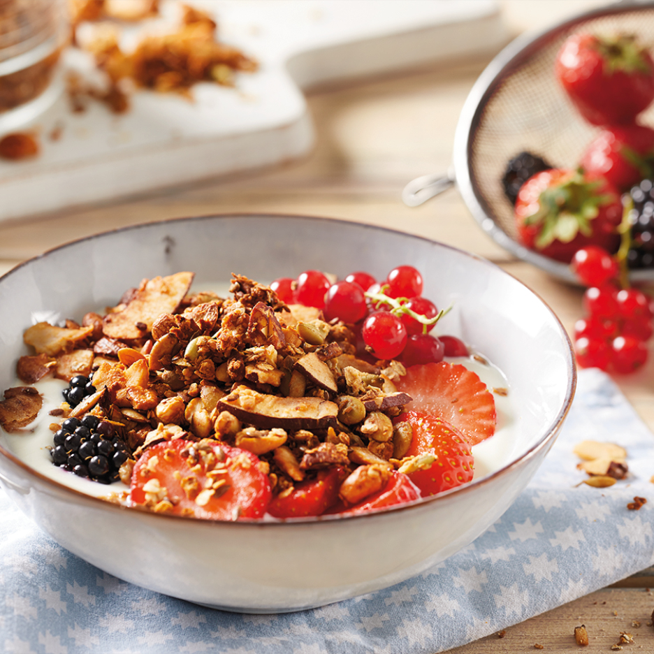 Ciotola di yogurt con granola, fragole, ribes rossi e more su un tavolo di legno.