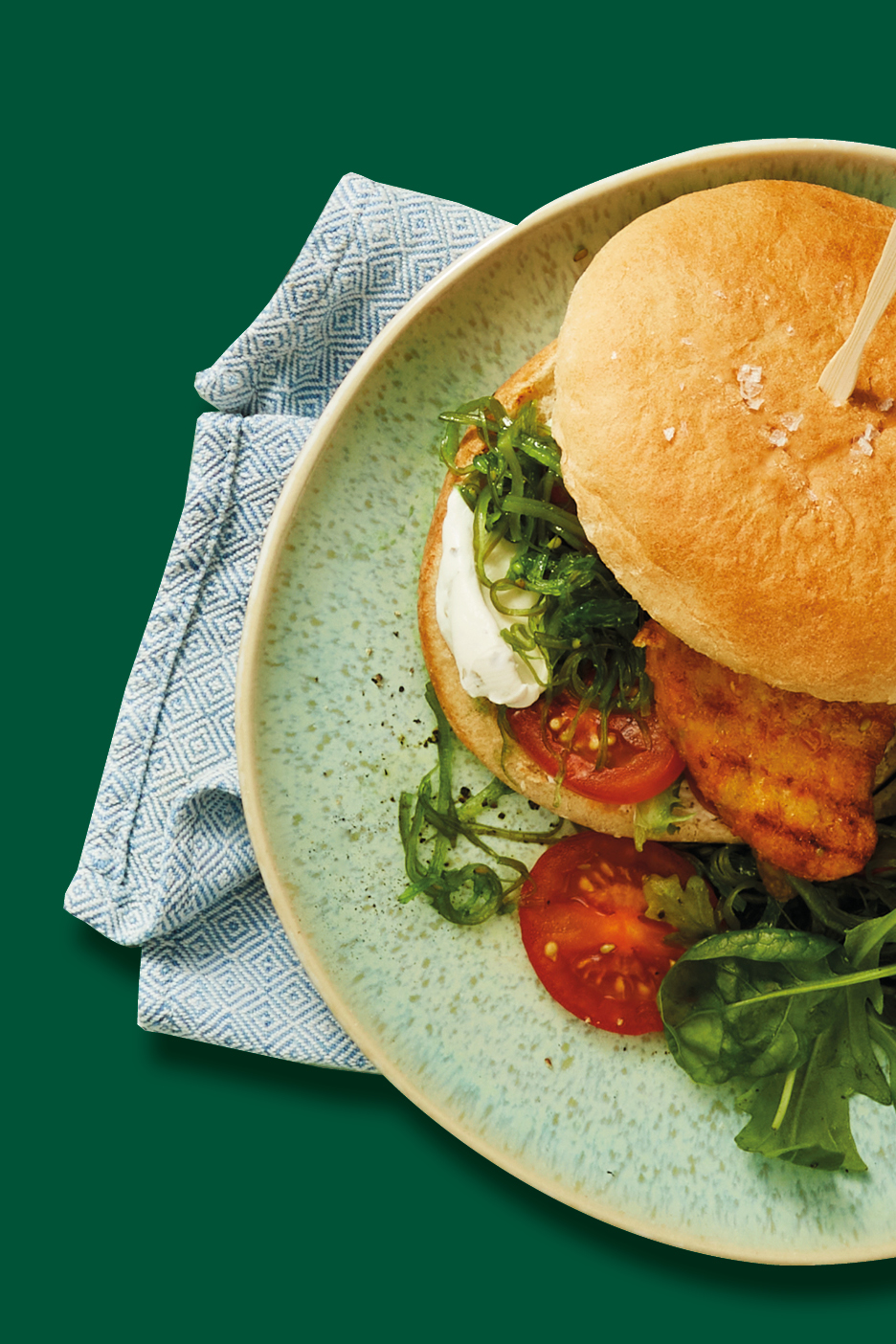 Hamburger di pesce con alghe, pomodori e rucola su un piatto verde chiaro.