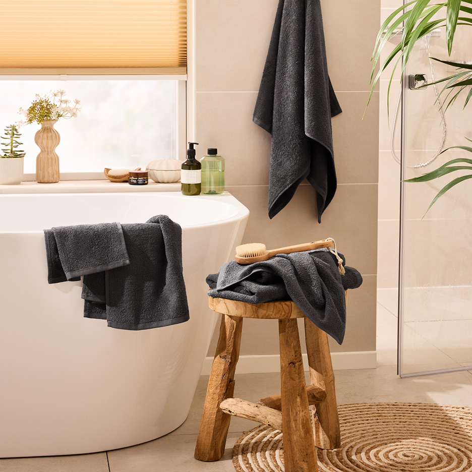 Asciugamani grigi in un bagno moderno con vasca, sgabello in legno e piante.