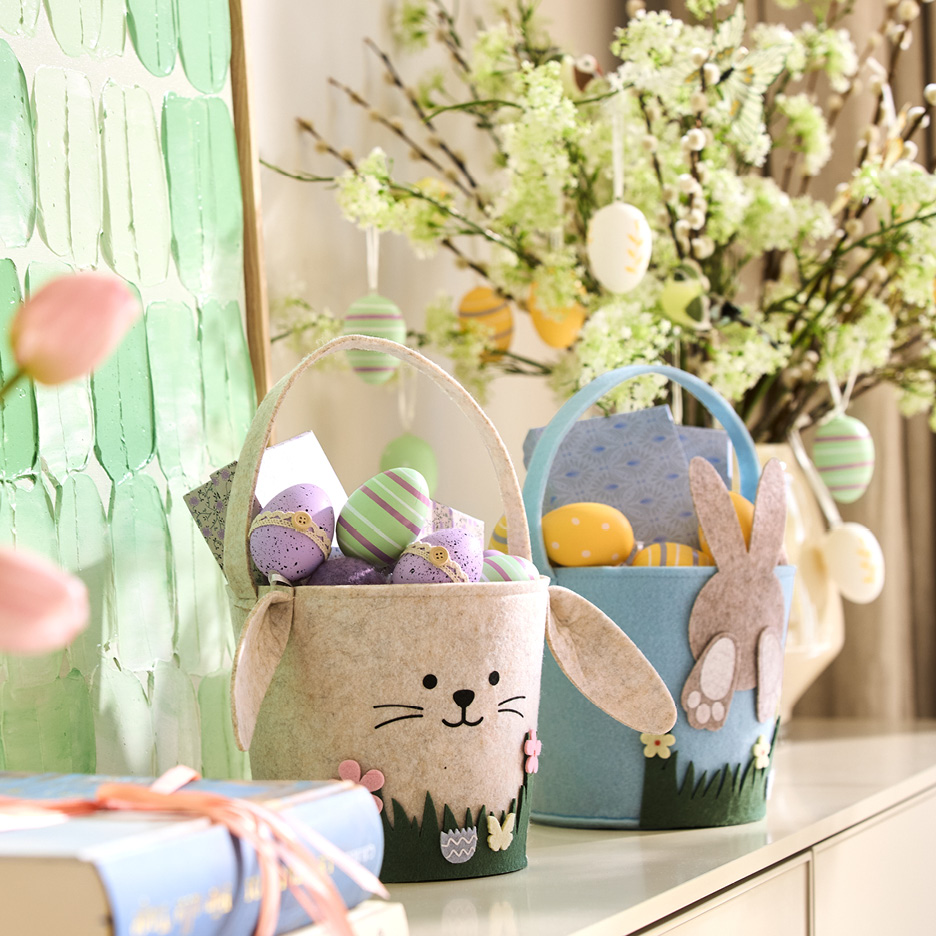 Cesti pasquali in feltro a forma di coniglio con uova colorate, su un tavolo con decorazioni primaverili.