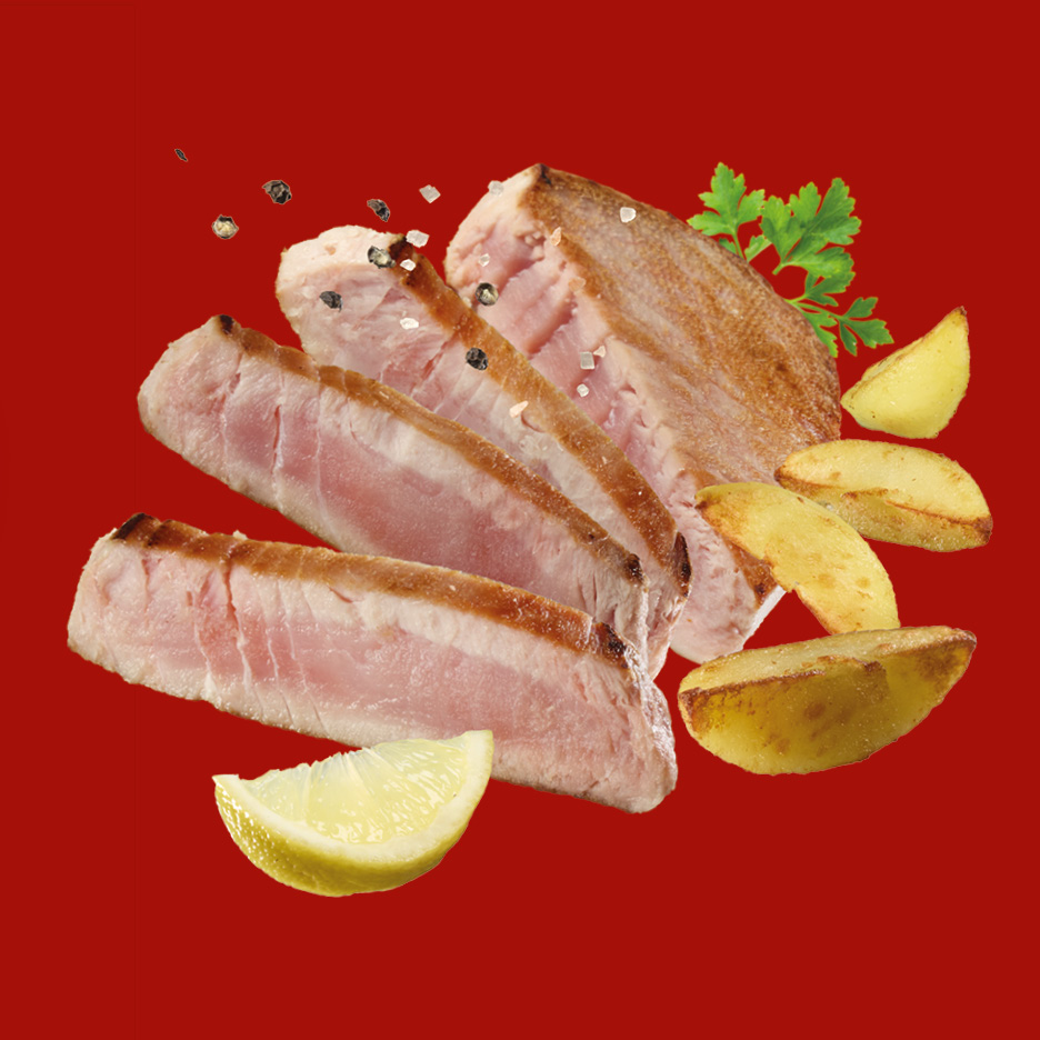 Tranci di tonno con patate al forno, limone e prezzemolo su sfondo rosso.