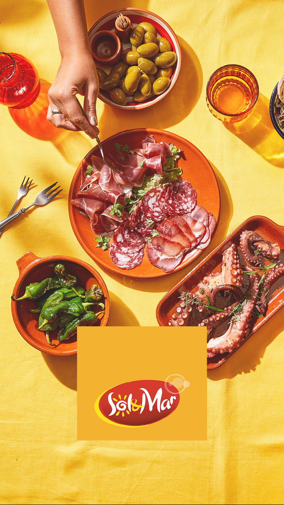 Tapas spagnole con salumi, polpo, peperoni e olive su un tavolo giallo.