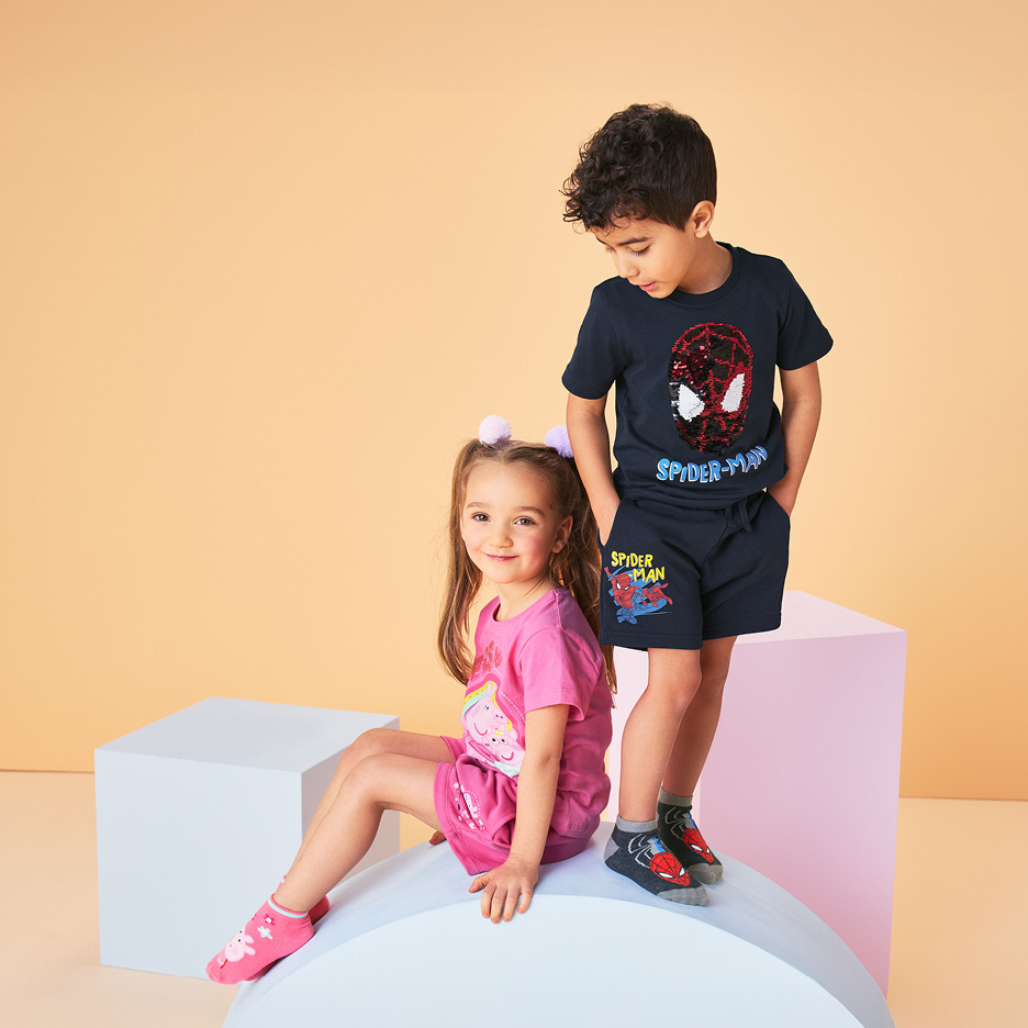 Bambini in pigiami estivi: un bambino con un pigiama blu con motivo di supereroe, una bambina con un pigiama rosa con motivo di maialino.