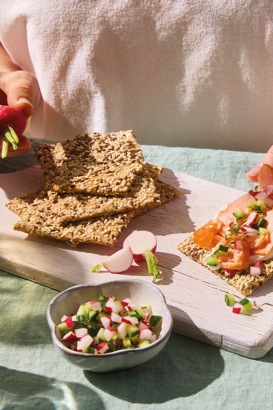 Cracker di semi con salmone affumicato, formaggio spalmabile e insalata di ravanelli e cetrioli.