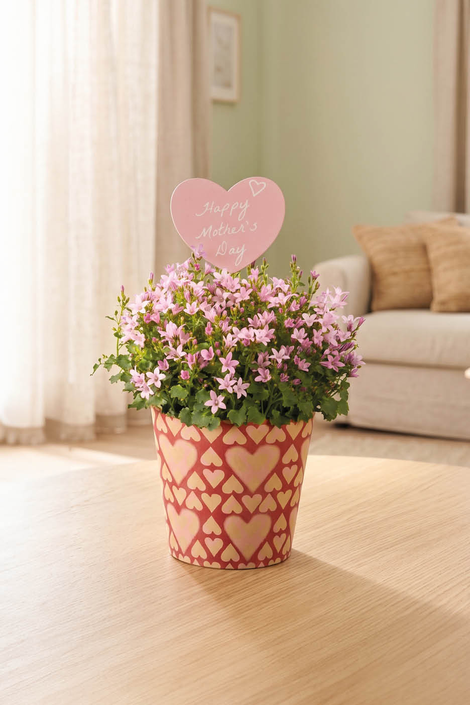 Vaso di fiori rosa con decorazione a cuore e scritta 'Happy Mother's Day' su un tavolo di legno.