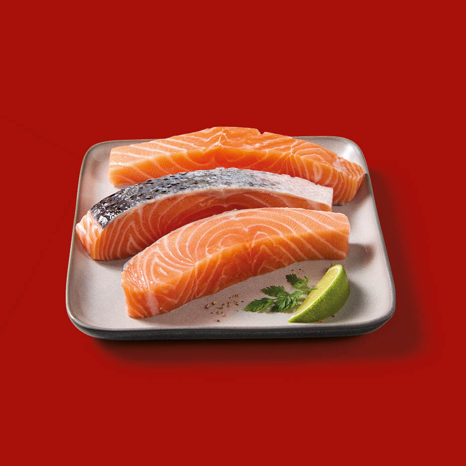 Tre filetti di salmone fresco su un piatto, guarniti con una fetta di lime e prezzemolo.