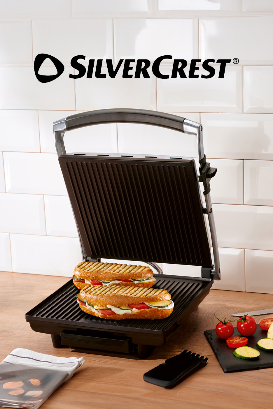 Piastra per panini aperta con due panini farciti e verdure fresche su un tagliere.