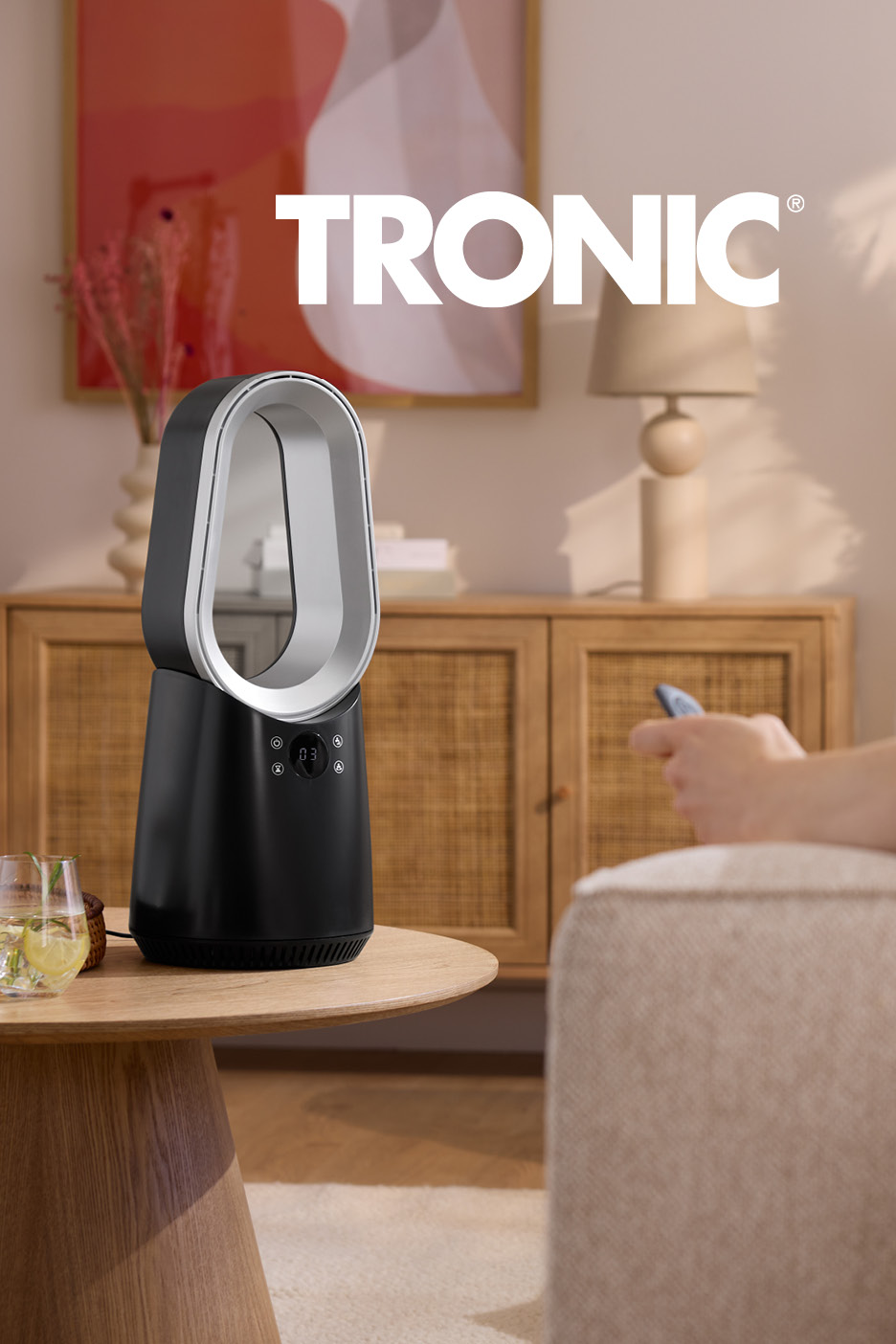 Ventilatore senza pale nero su tavolino in legno, persona sul divano con telecomando.