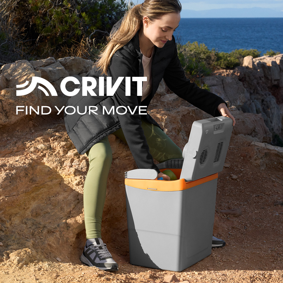 Donna in abbigliamento sportivo apre un frigo portatile in un paesaggio roccioso con il mare sullo sfondo. Testo: CRIVIT FIND YOUR MOVE.