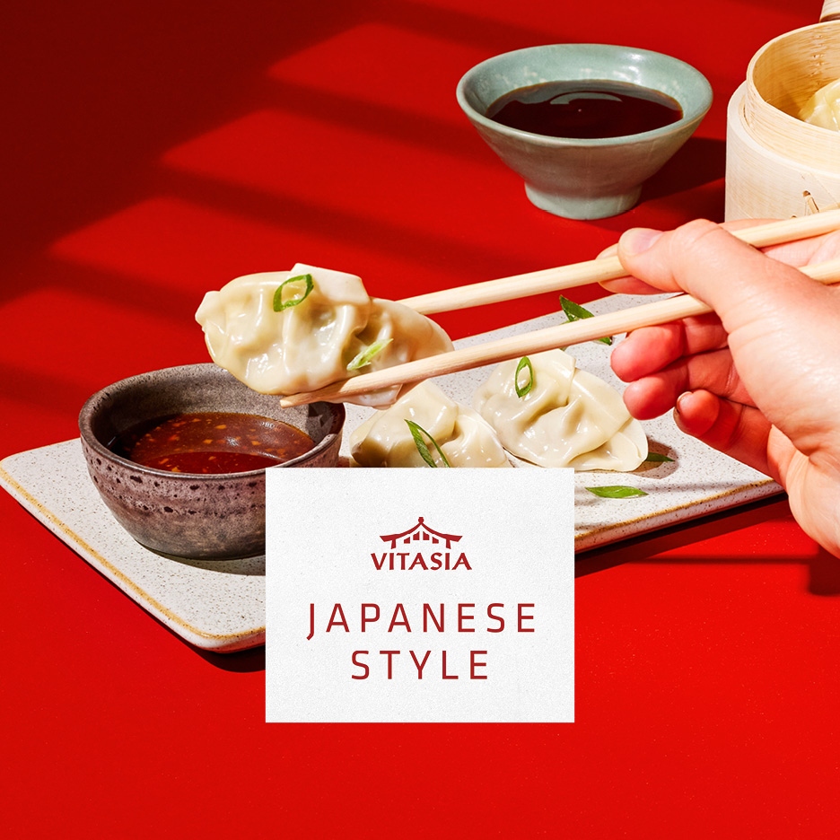Gyoza giapponesi con salsa, presi con le bacchette. Testo: 'JAPANESE STYLE'.
