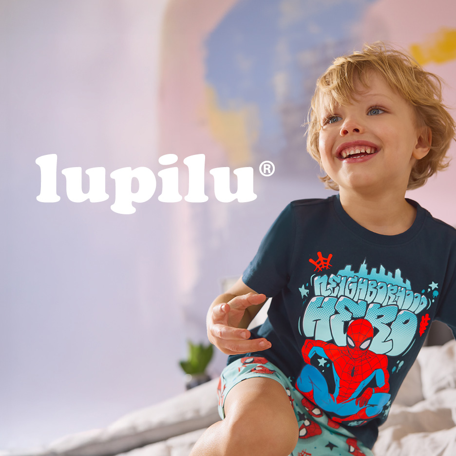 Bambino sorridente con maglietta e pantaloncini a tema supereroe.