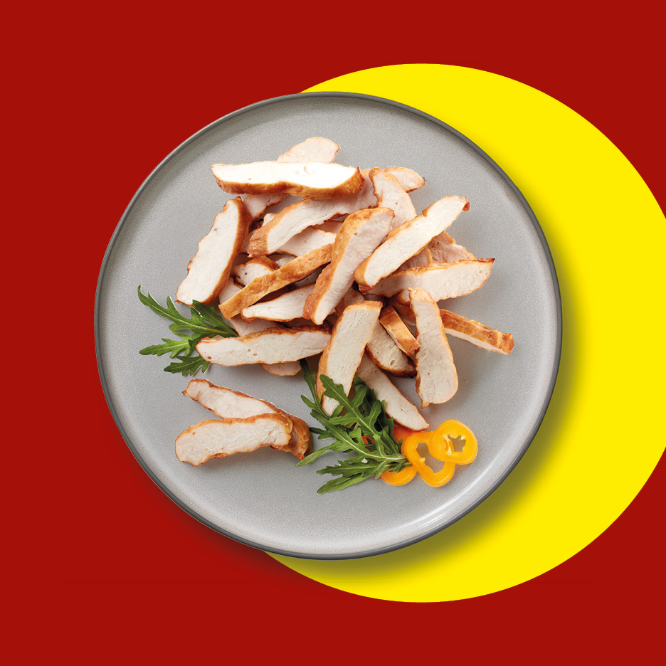 Fettine di pollo cotto con rucola e peperoni gialli su un piatto grigio, sfondo rosso e giallo.