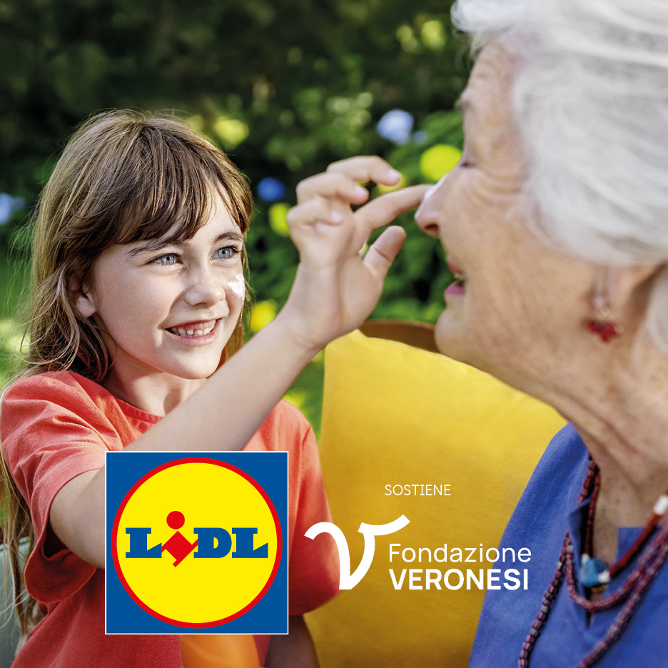 Una bambina applica la crema solare sul naso di una donna anziana, sorridendo.