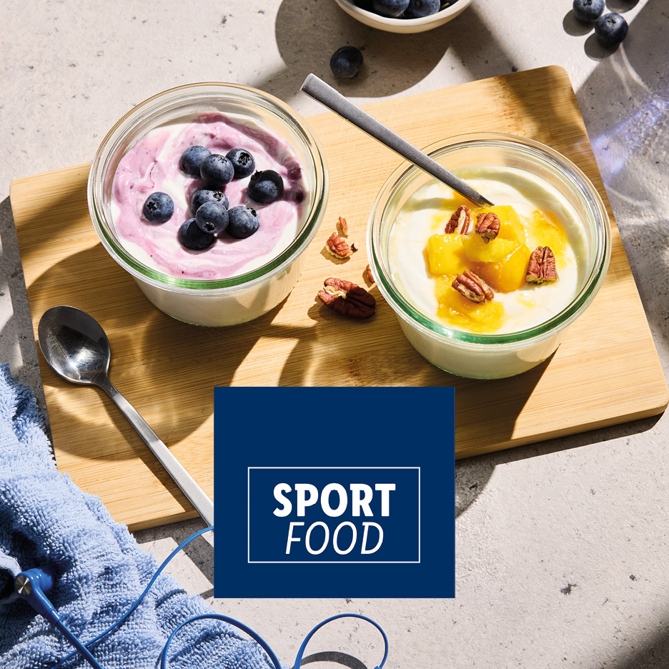 Due vasetti di yogurt con frutta e noci su un tagliere, con la scritta 'SPORT FOOD'.