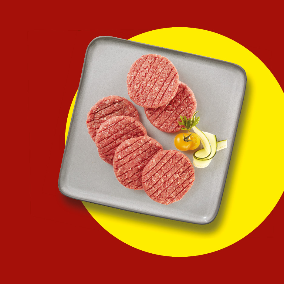 Hamburger di carne cruda su un piatto grigio con pomodoro e zucchine, su sfondo rosso e giallo.