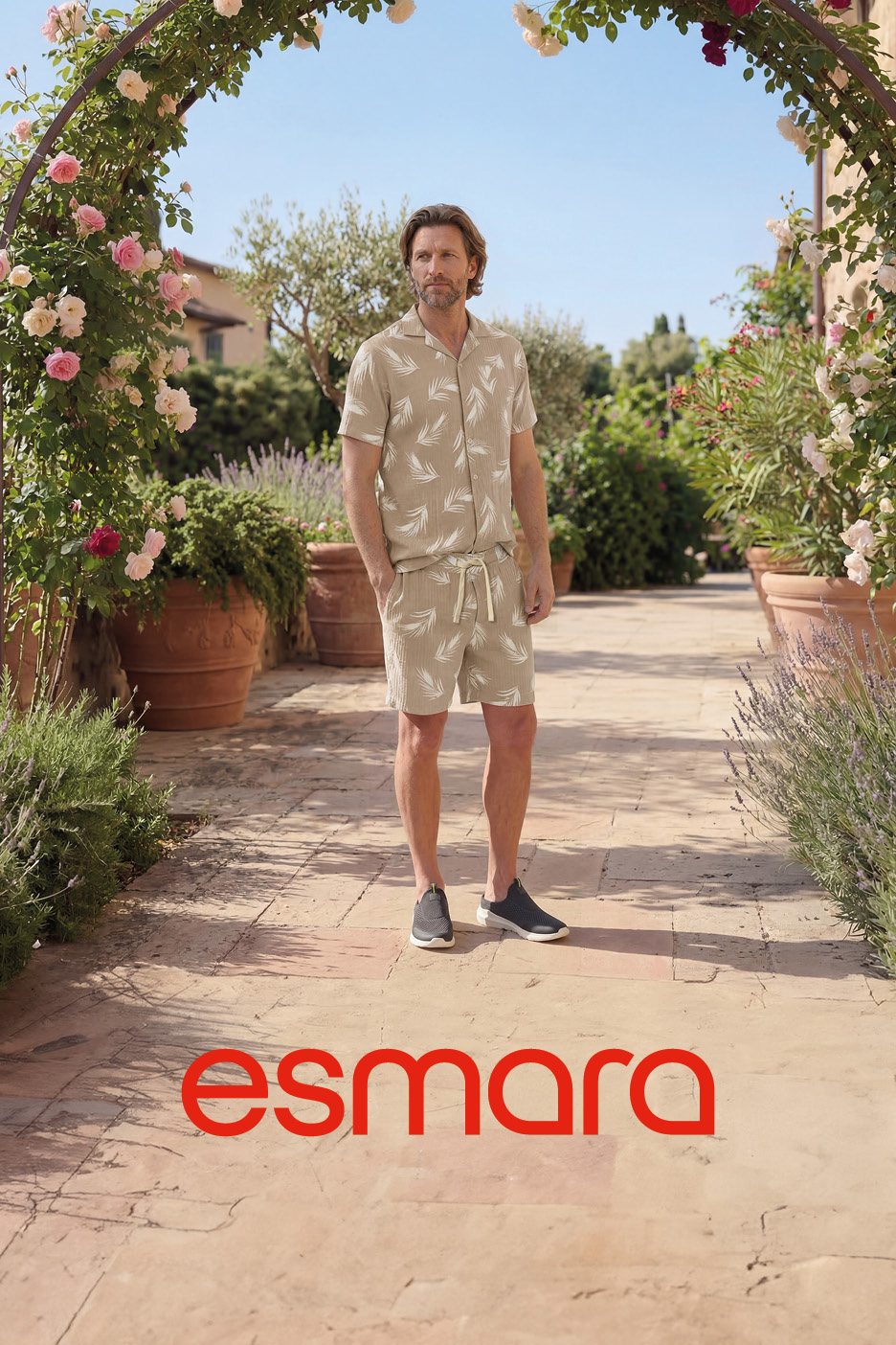 Uomo in completo estivo beige con stampa a foglie, in un giardino fiorito con arco di rose.