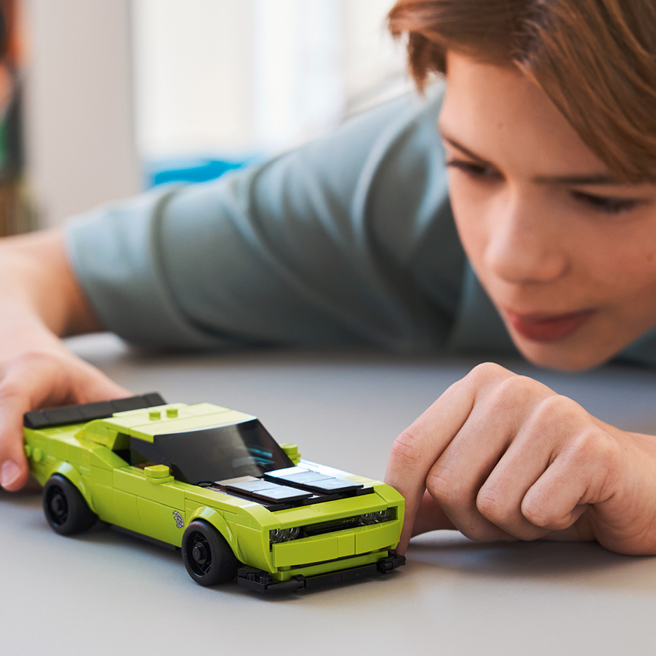 Ragazzo che gioca con un'auto giocattolo verde brillante sul pavimento.