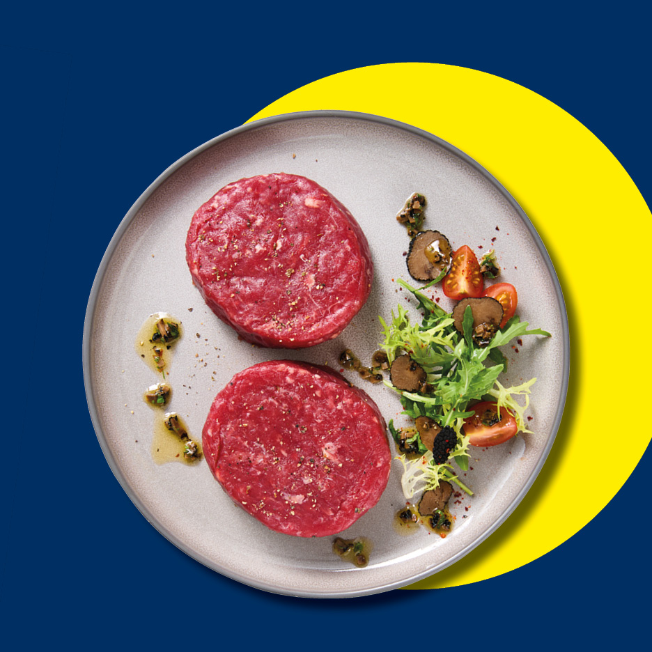 Due hamburger di manzo crudi con insalata, pomodorini e scaglie di tartufo su un piatto.